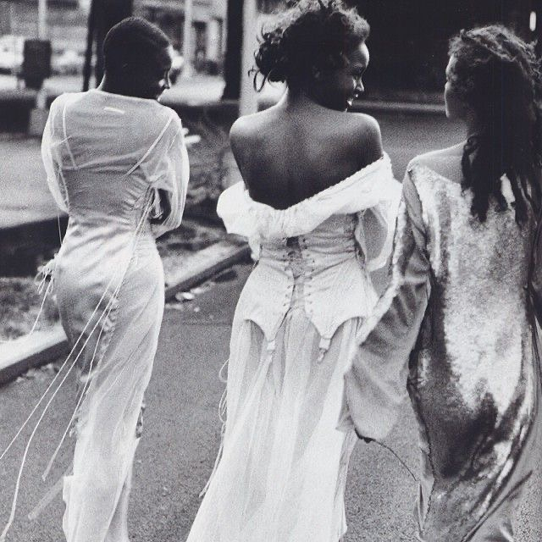 Three women in elegant dresses walking together on a street.