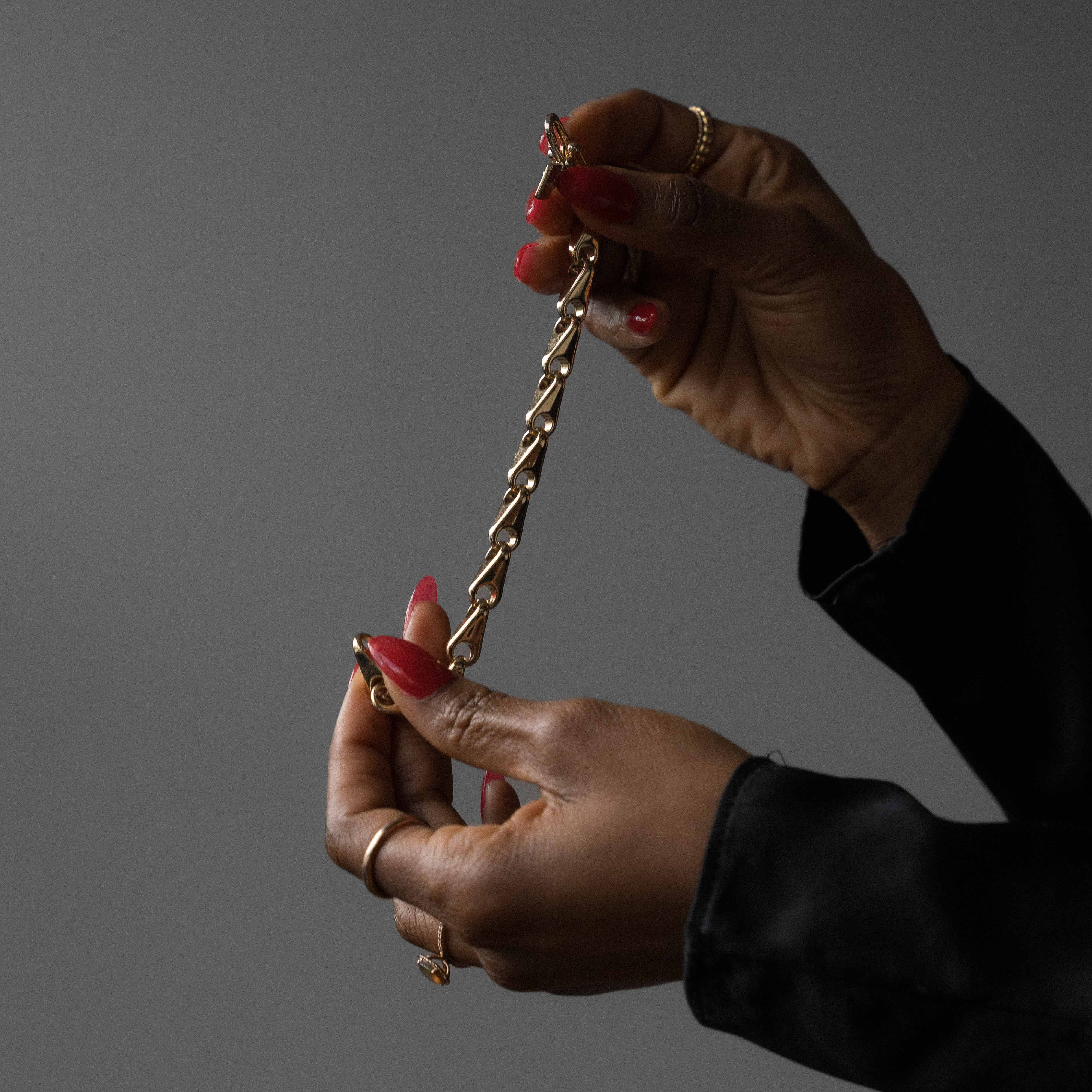 image of a woman with classic red nails holding a gold bracelet