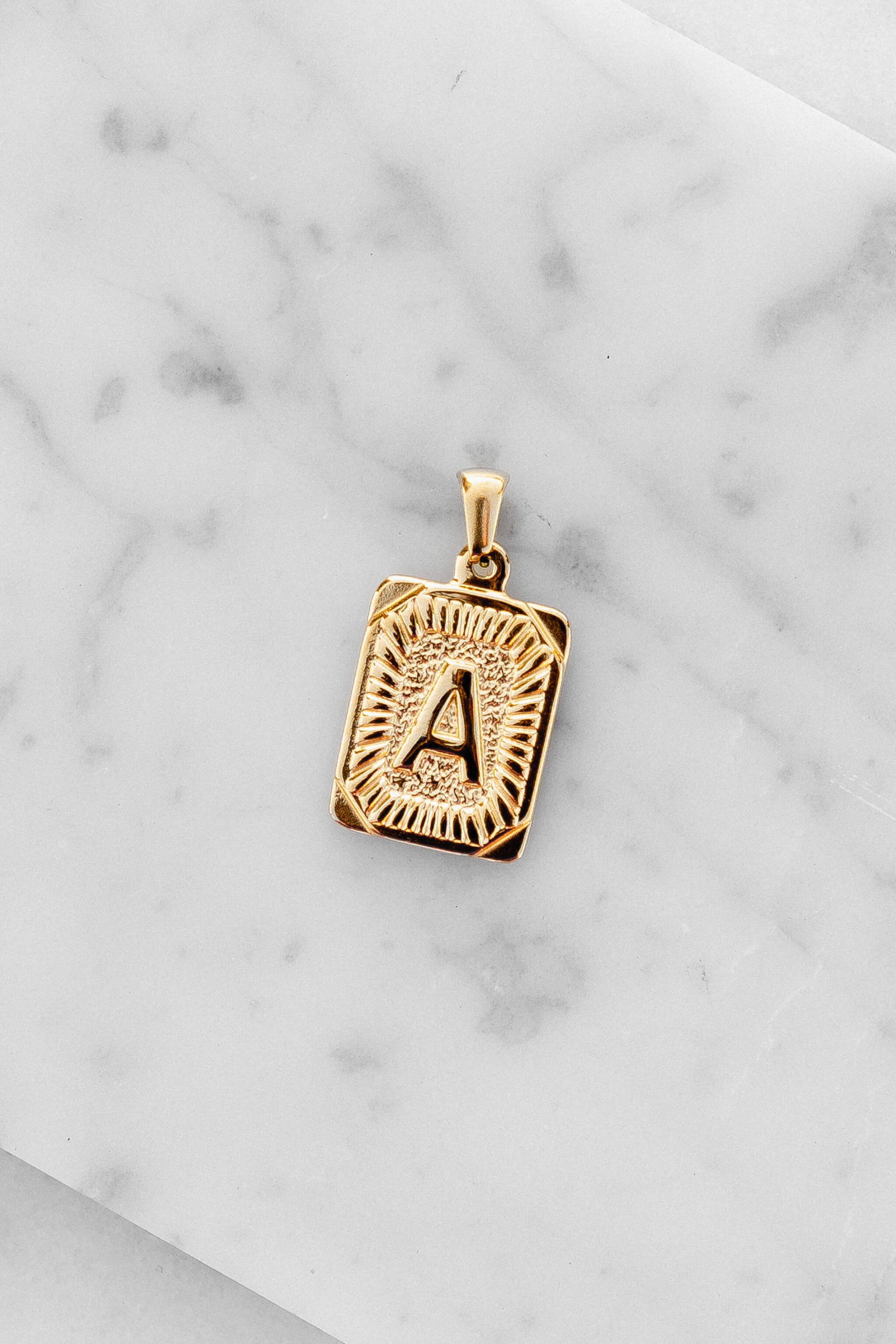 Gold Monogram Letter "A" Charm laying on a marble