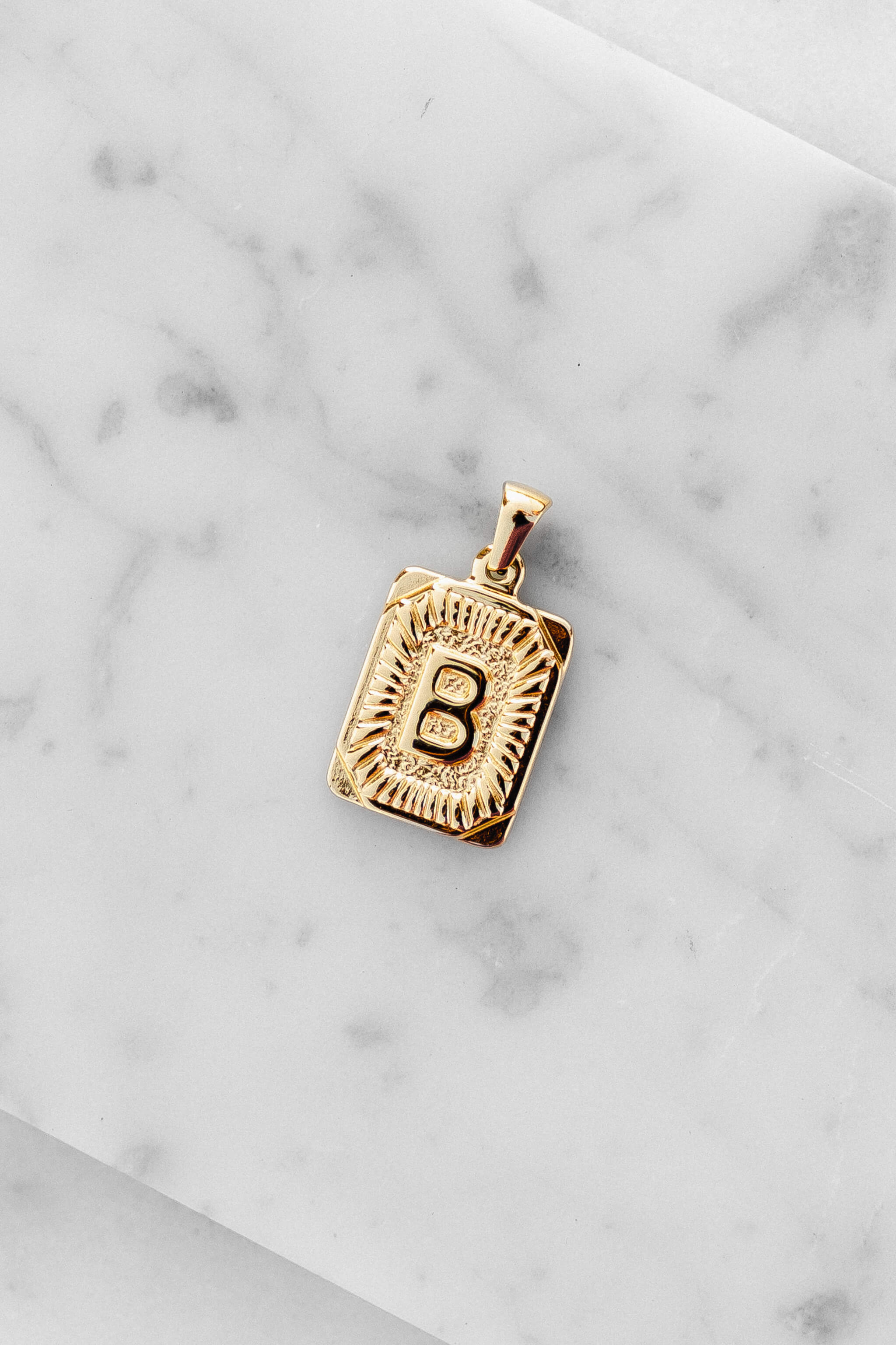 Gold Monogram Letter "B" Charm laying on a marble