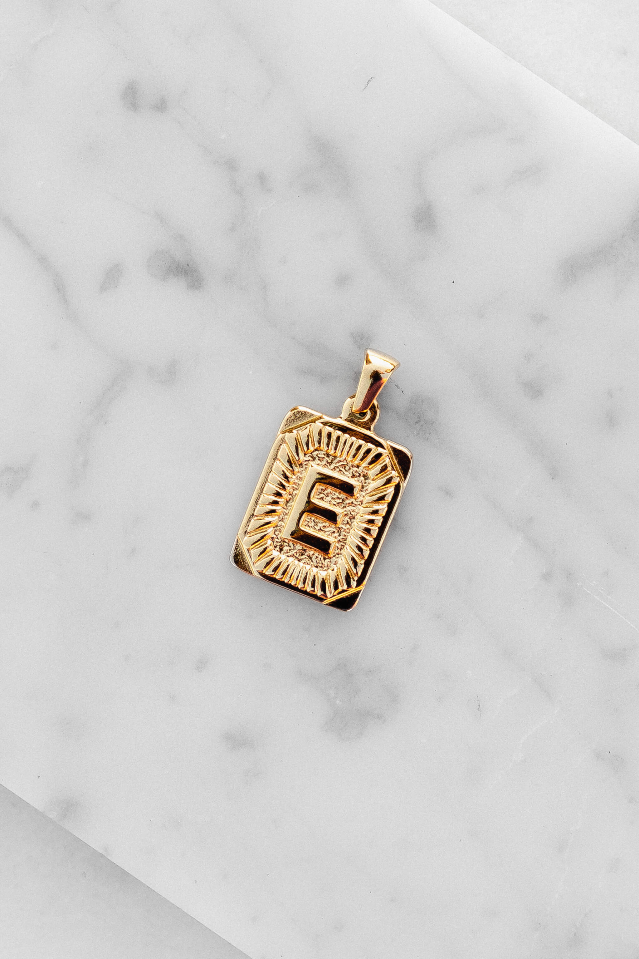 Gold Monogram Letter "E" Charm laying on a marble