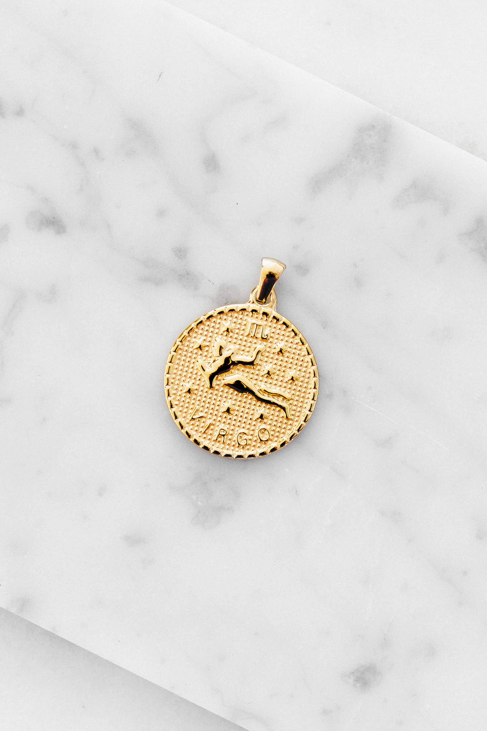 Virgo zodiac sign gold coin charm laying on a white marble
