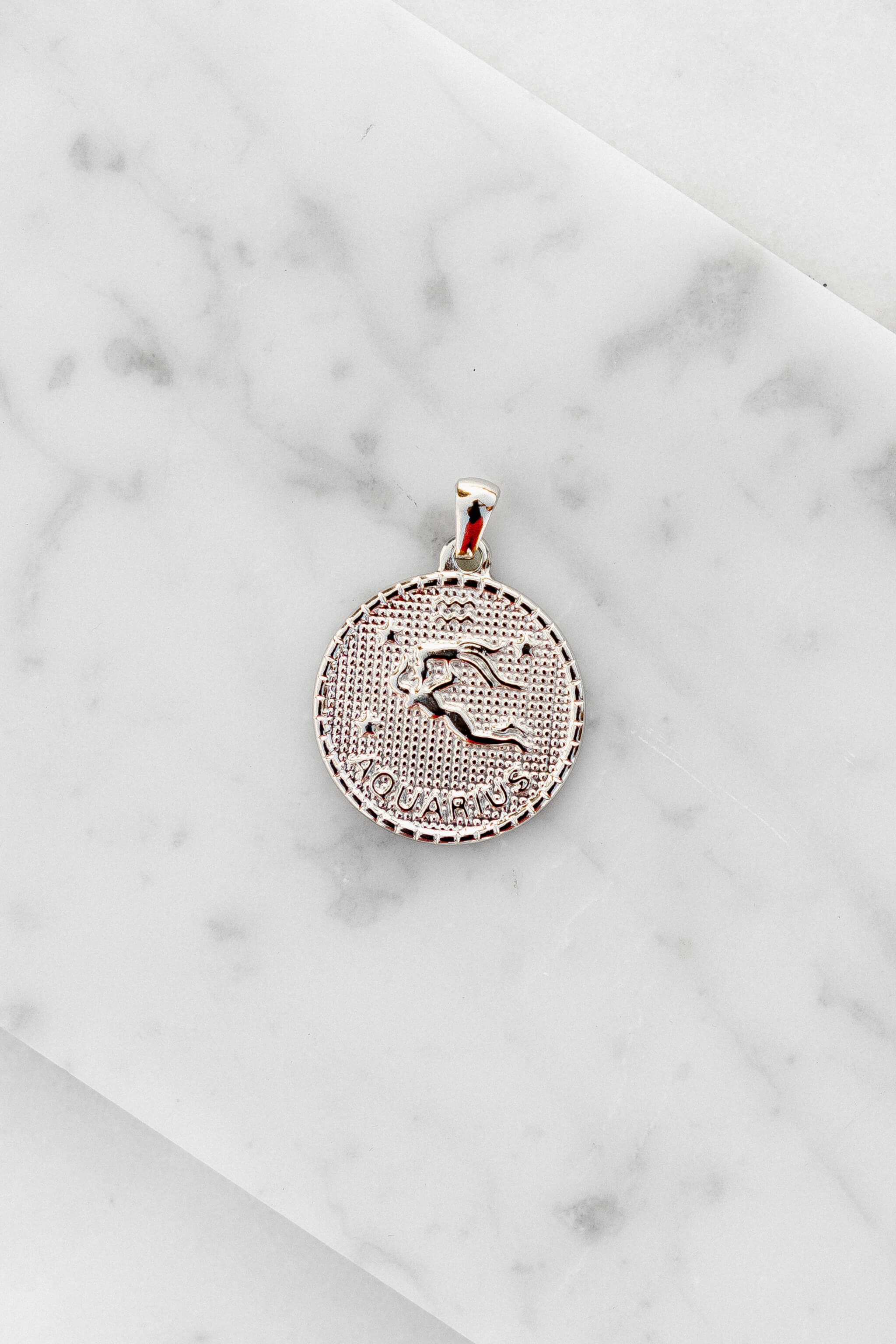 Aquarius zodiac sign silver coin charm laying on a white marble