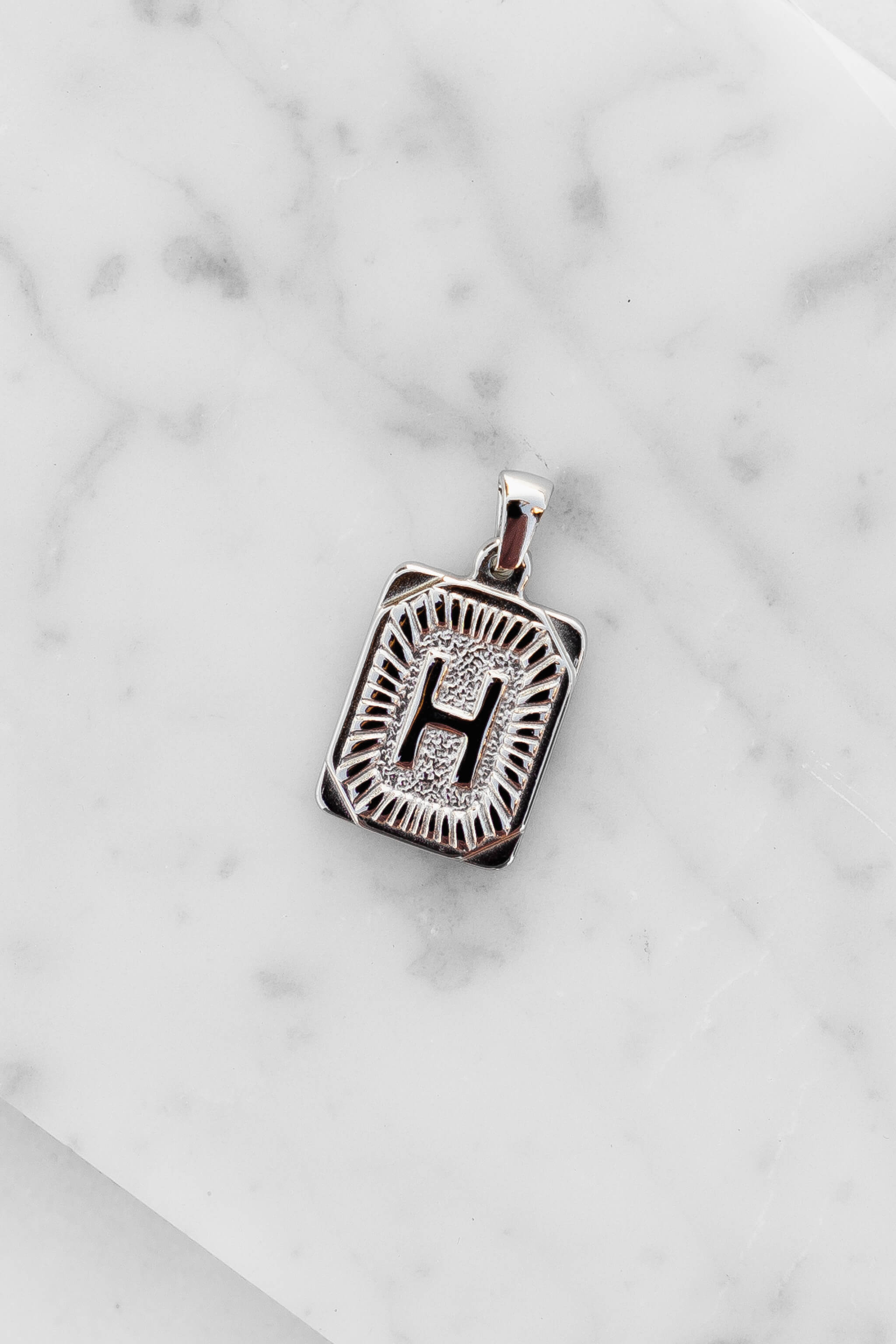 Silver Monogram Letter "H" Charm laying on a marble
