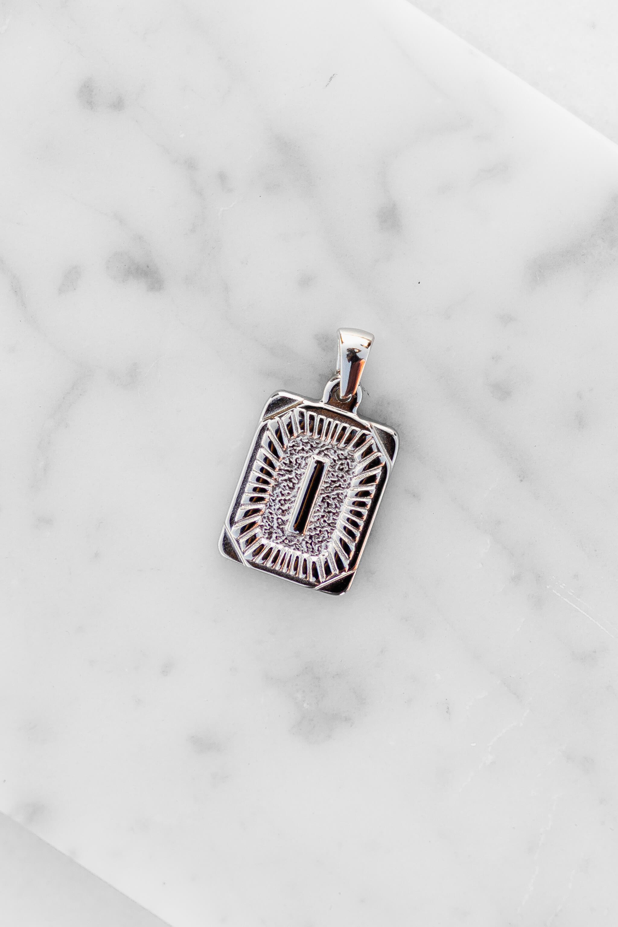 Silver Monogram Letter "I" Charm laying on a marble