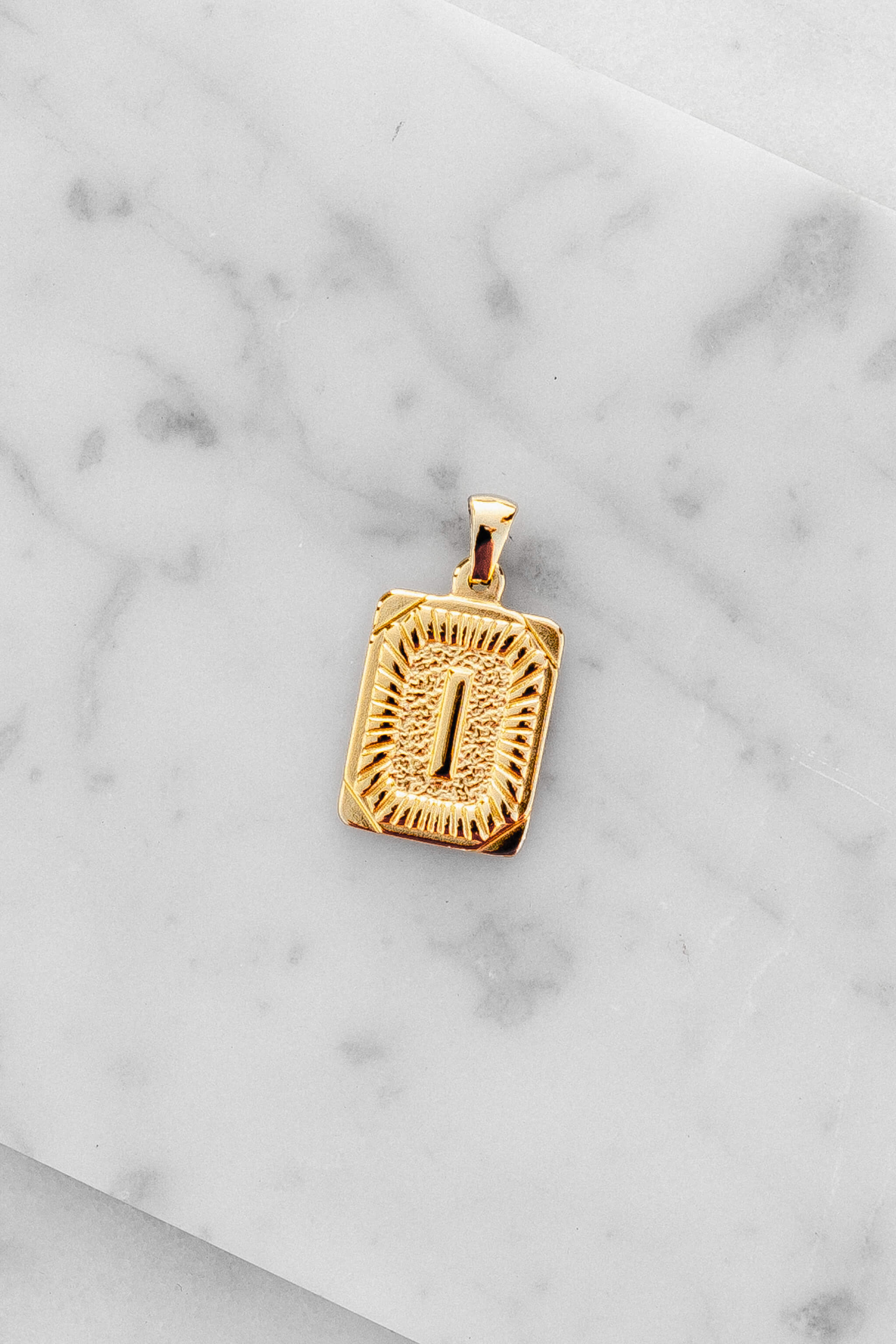 Gold Monogram Letter "I" Charm laying on a marble