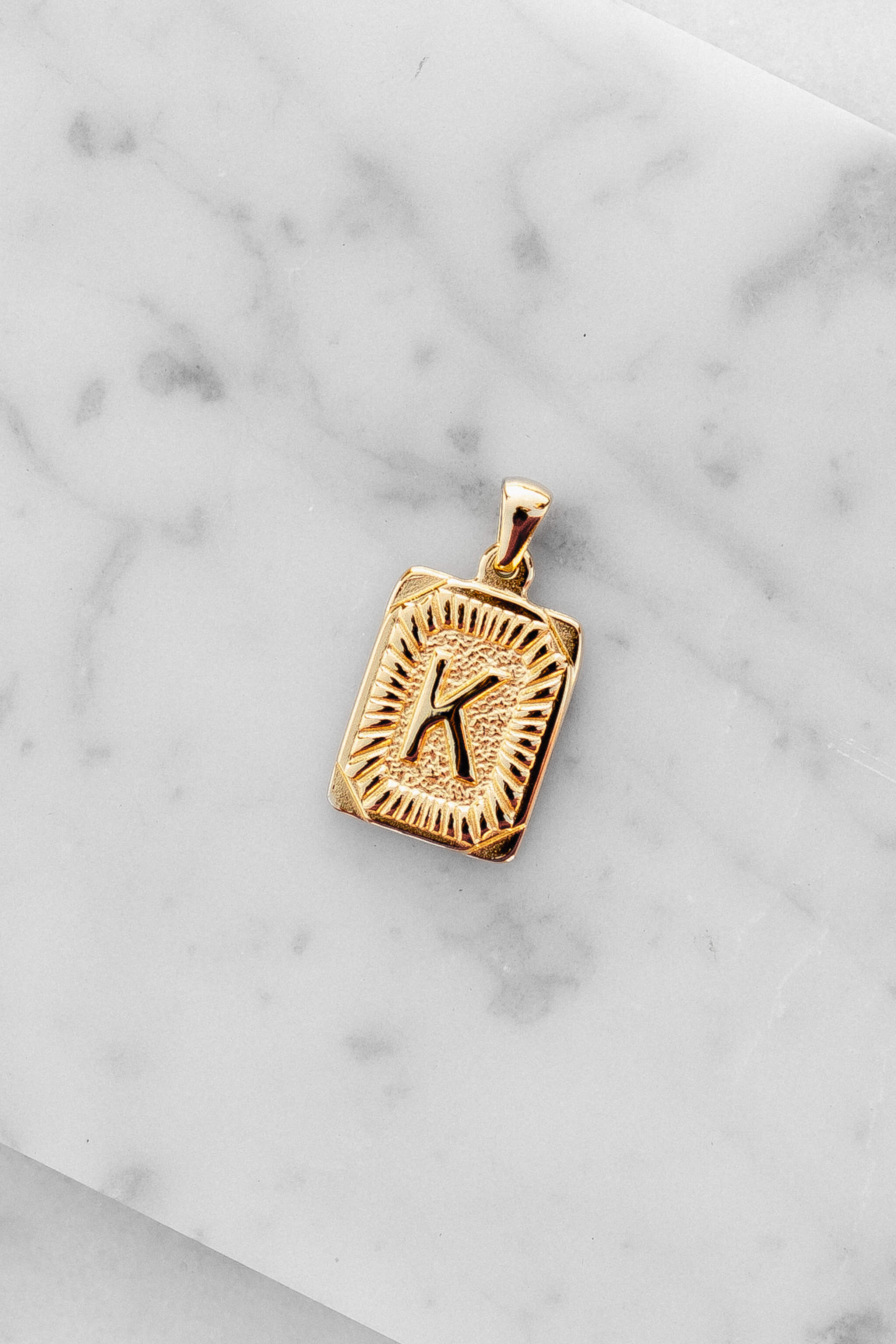 Gold Monogram Letter "K" Charm laying on a marble