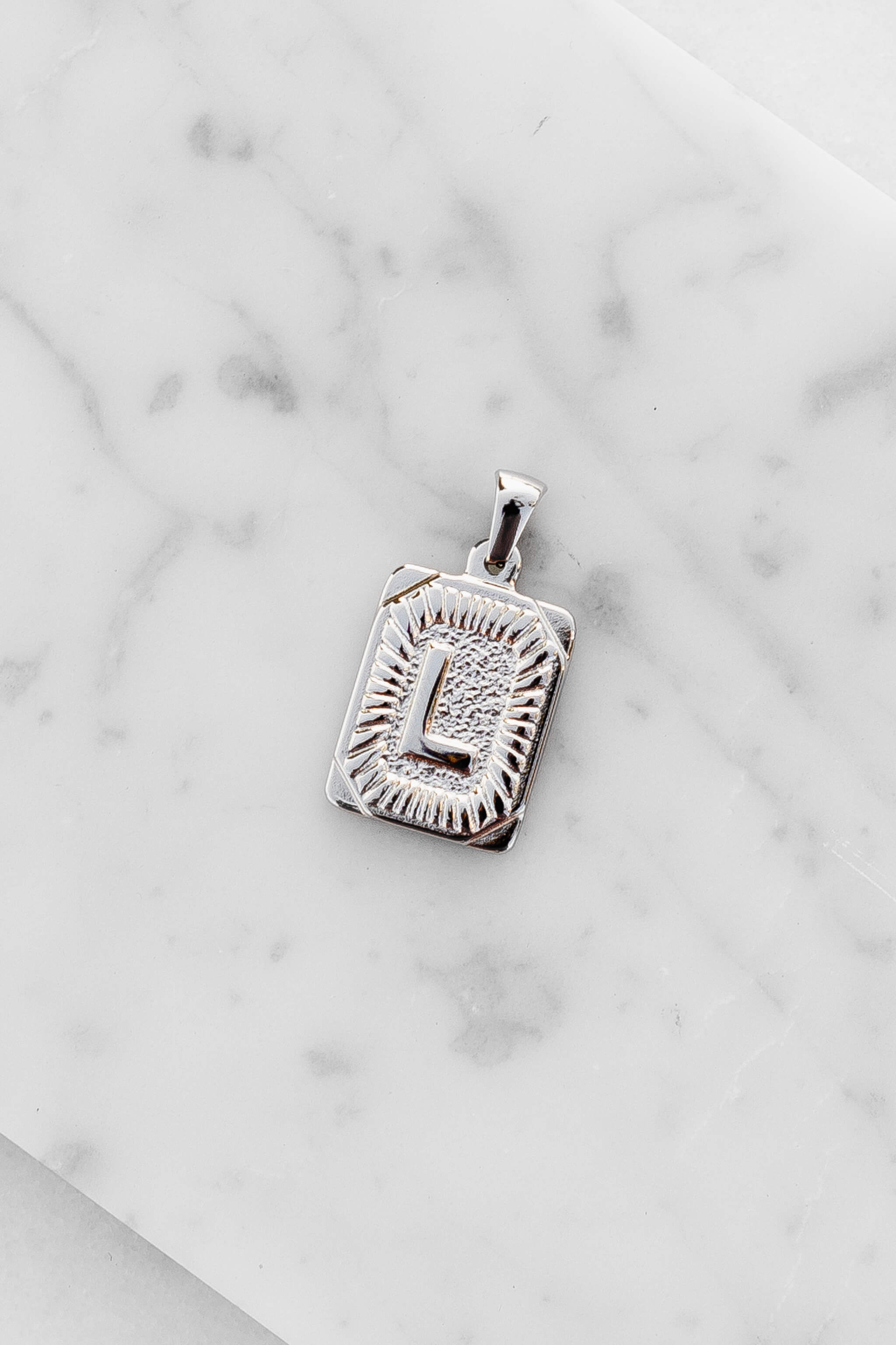 Silver Monogram Letter "L" Charm laying on a marble