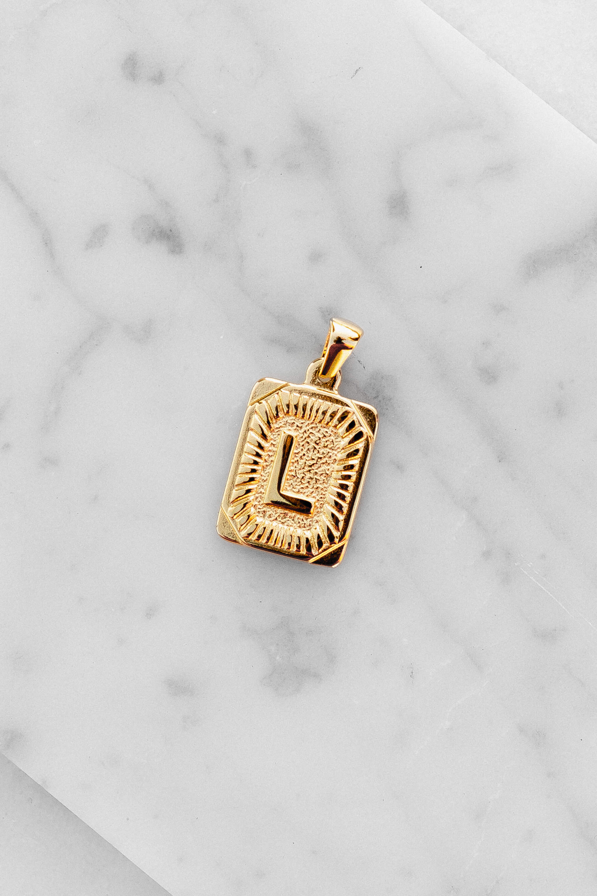 Gold Monogram Letter "L" Charm laying on a marble