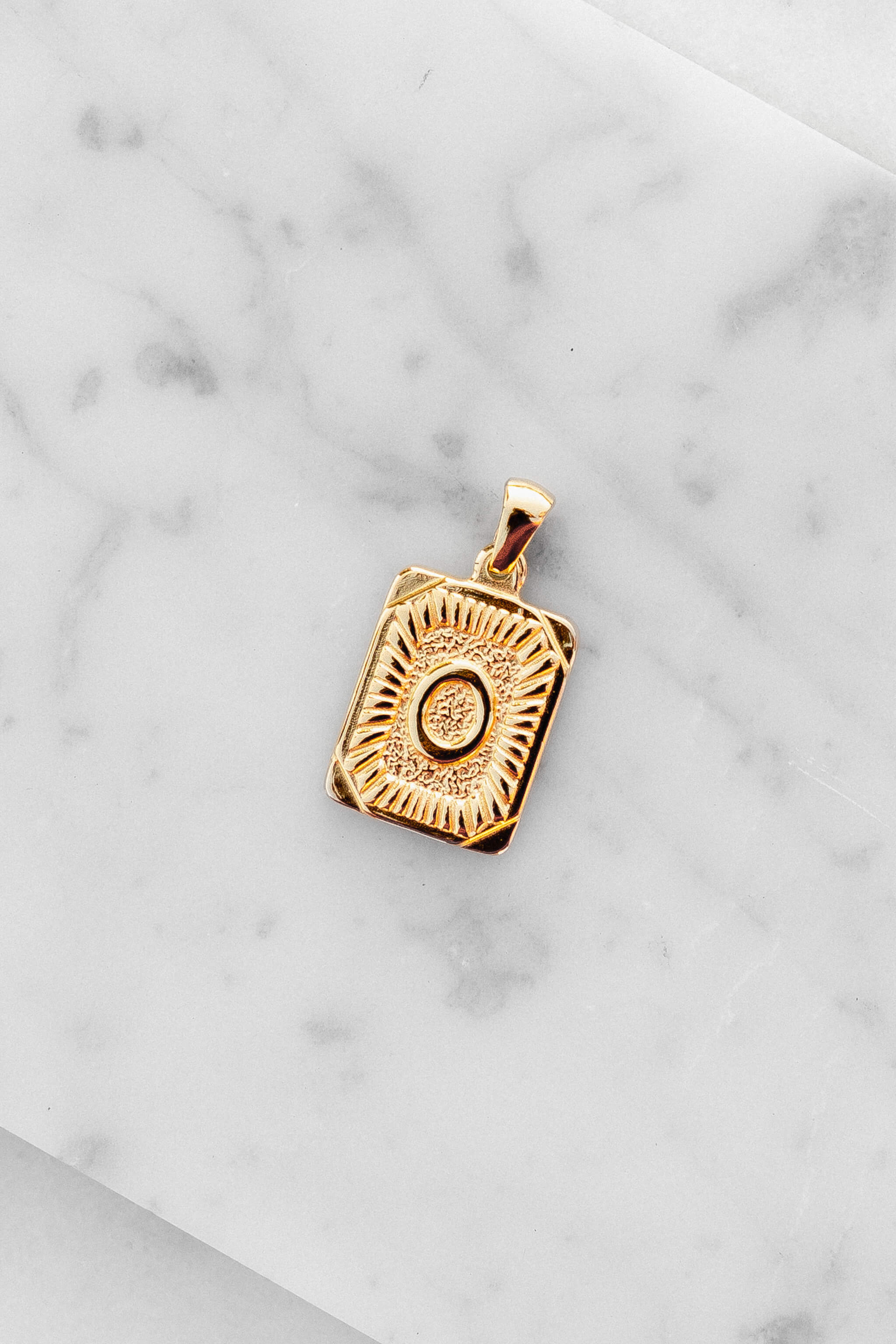 Gold Monogram Letter "O" Charm laying on a marble