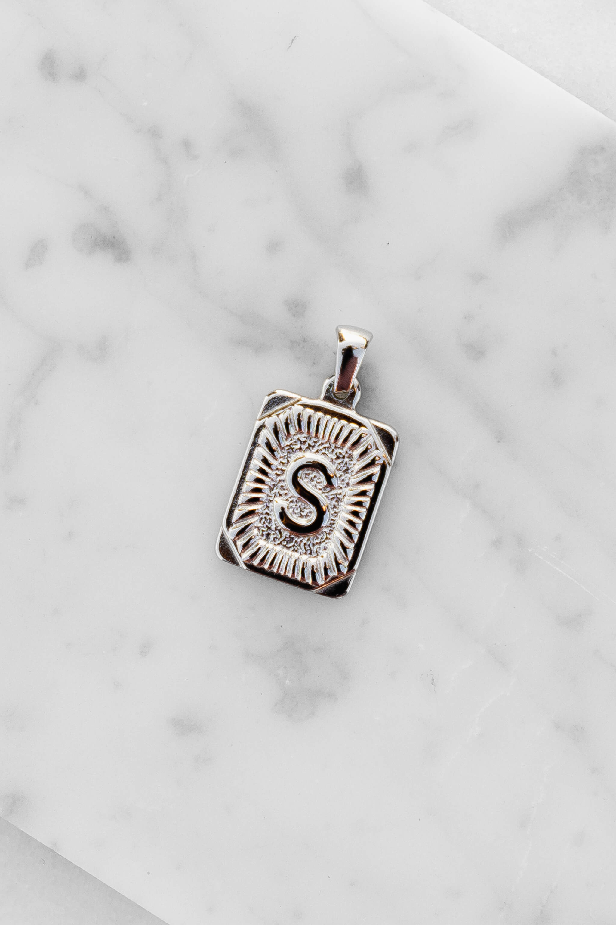 Silver Monogram Letter "S" Charm laying on a marble