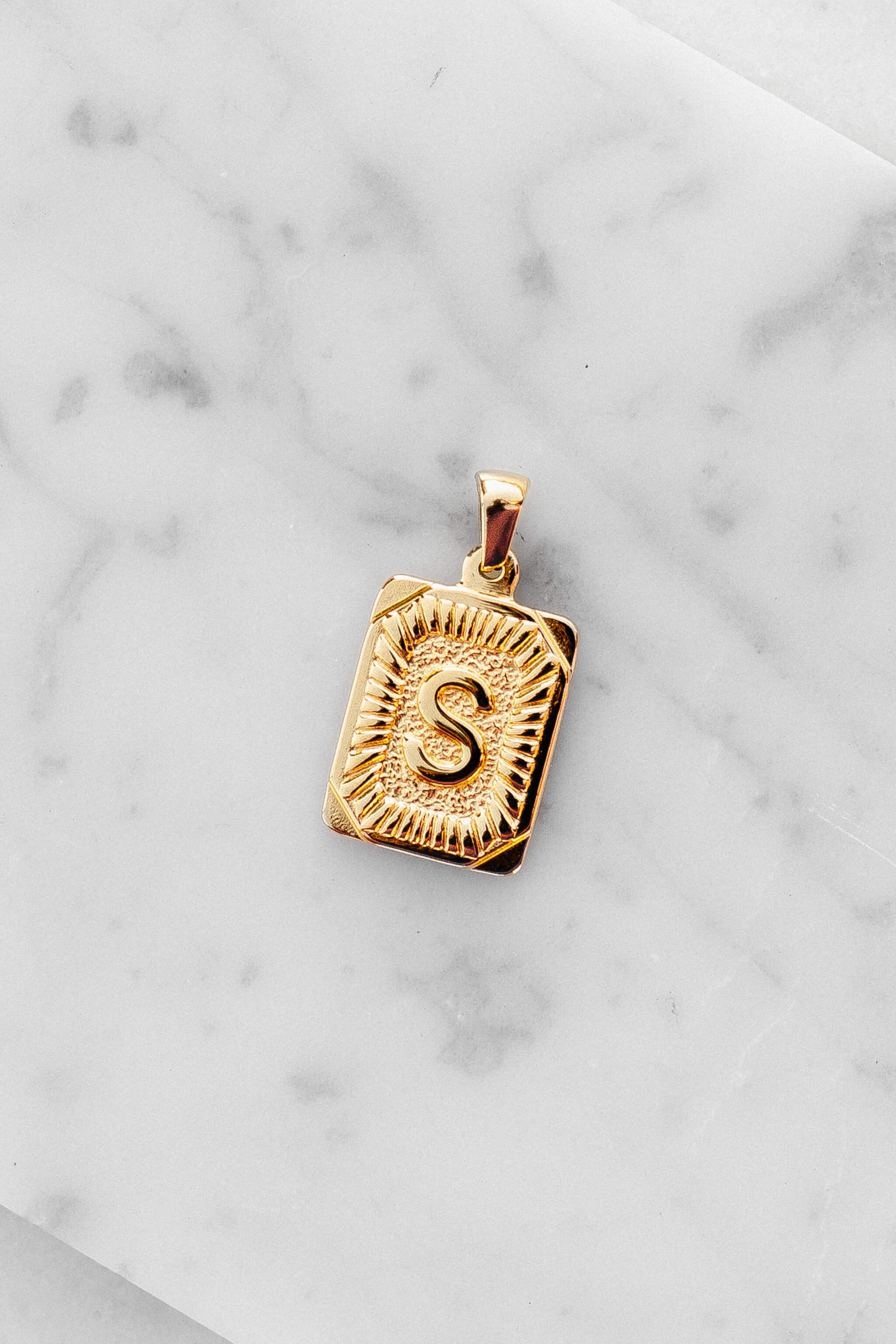 Gold Monogram Letter "S" Charm laying on a marble