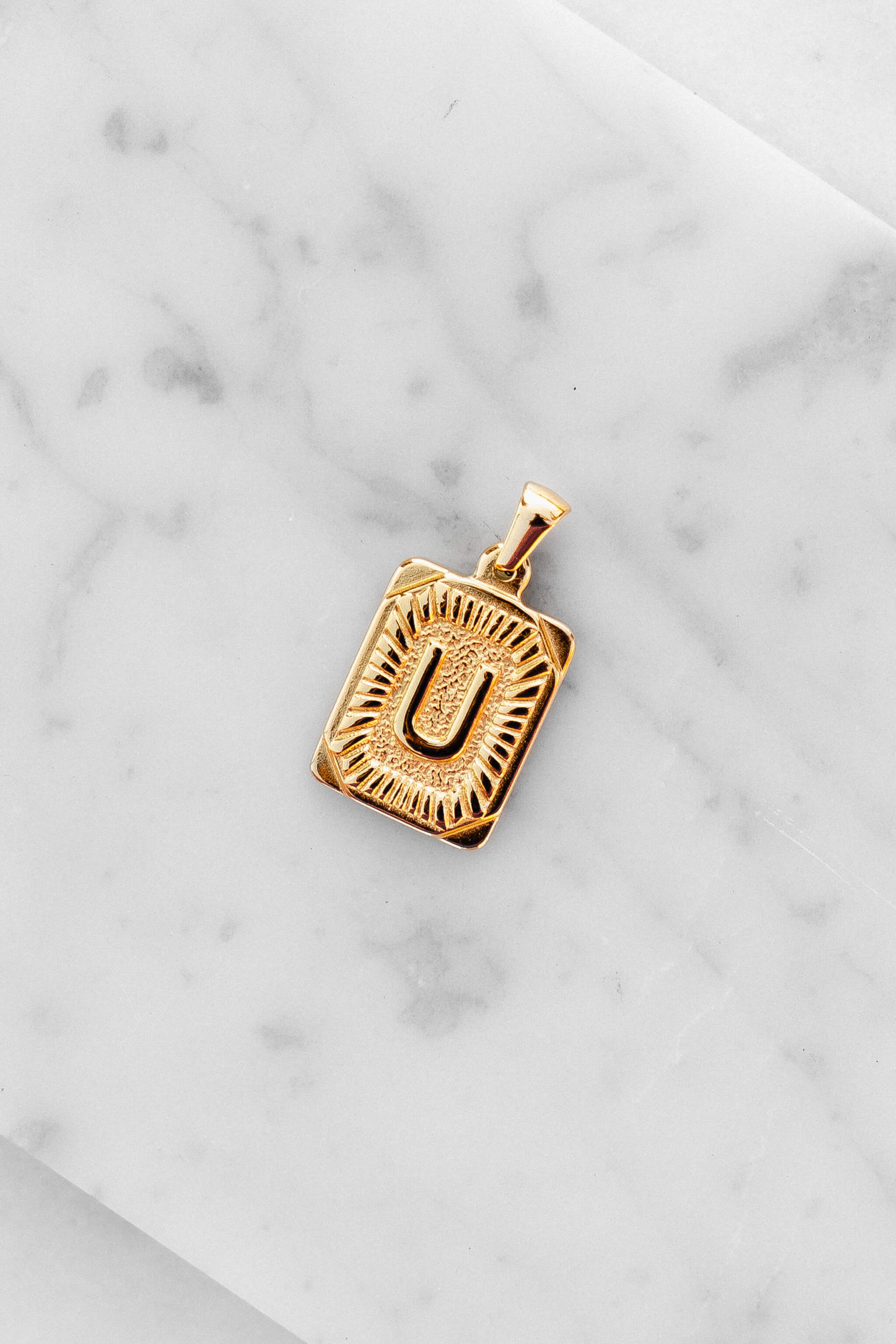 Gold Monogram Letter "U" Charm laying on a marble