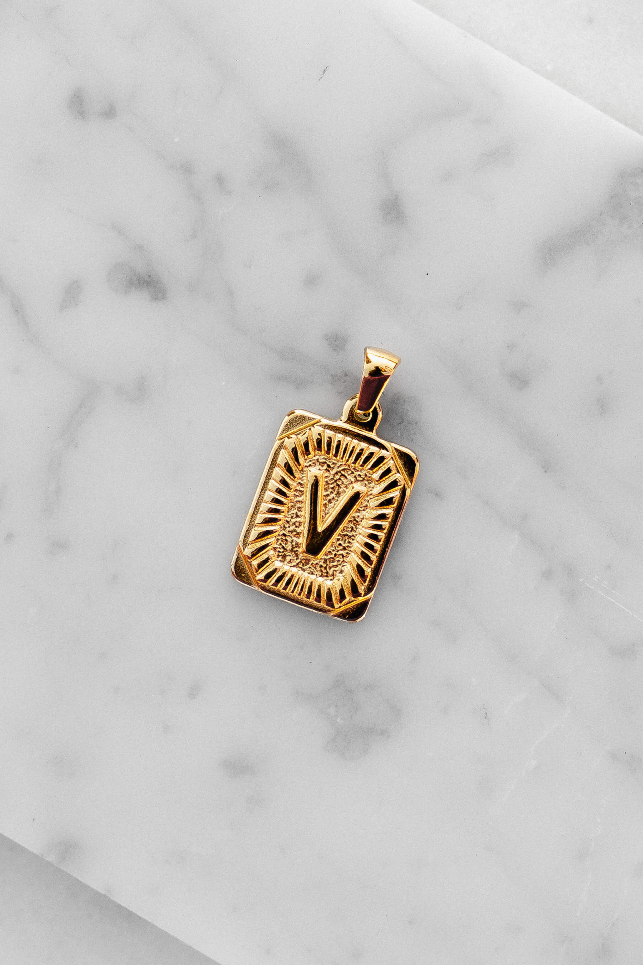 Gold Monogram Letter "V" Charm laying on a marble