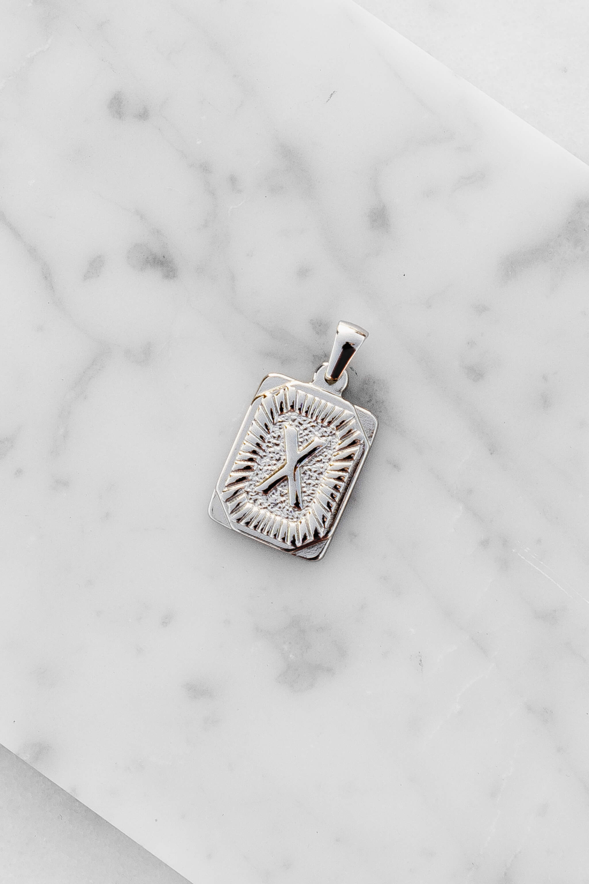 Silver Monogram Letter "X" Charm laying on a marble