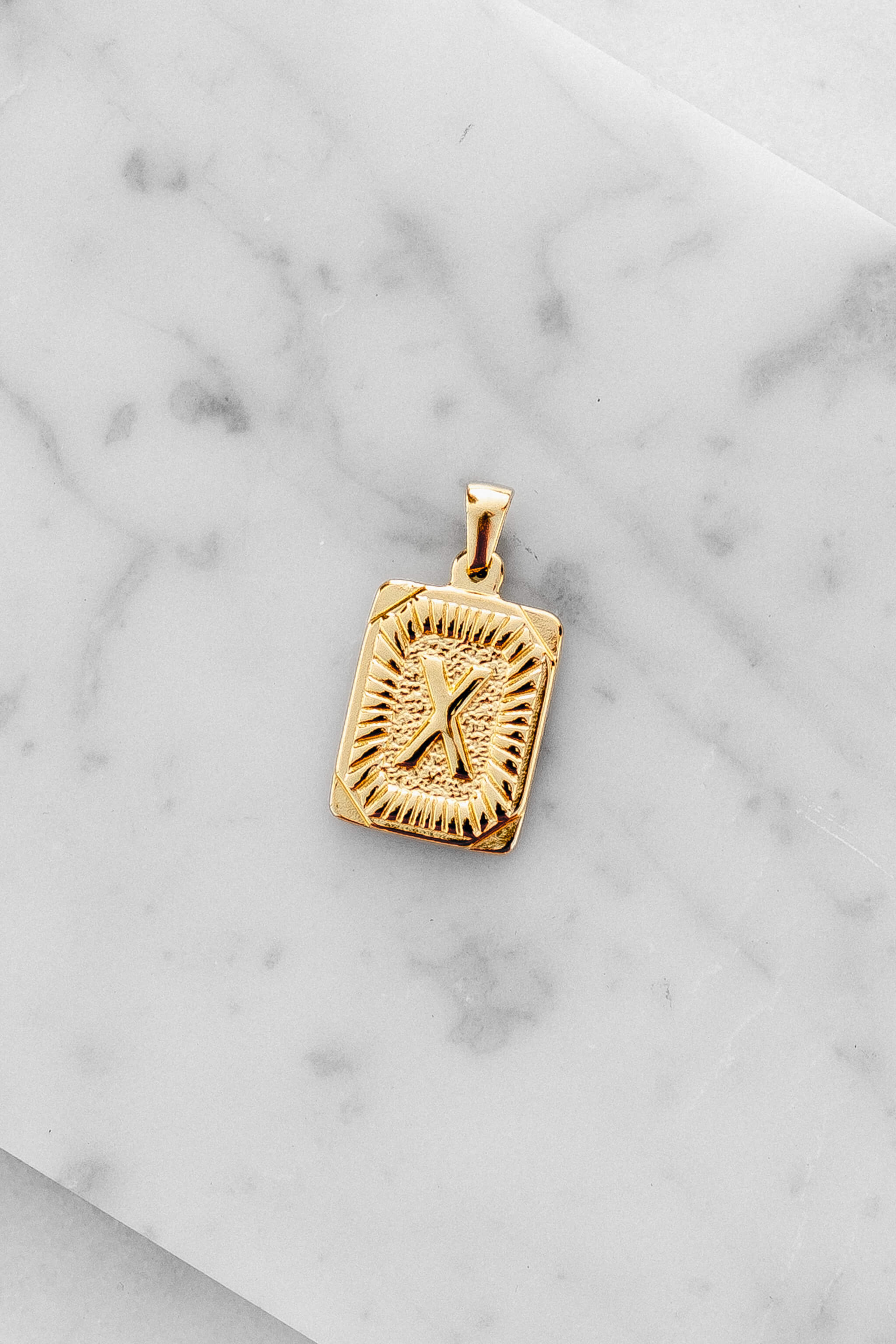 Gold Monogram Letter "X" Charm laying on a marble