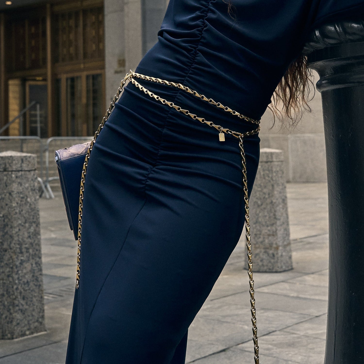 Gold chain belt with a small tag by Lapo Lounge, styled on a navy blue ruched dress.