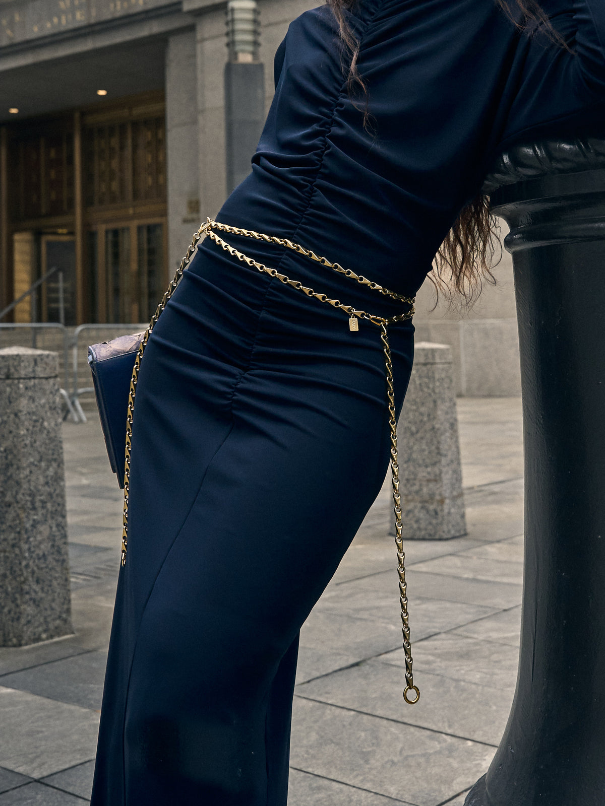Gold chain belt with a small tag by Lapo Lounge, styled on a navy blue ruched dress.