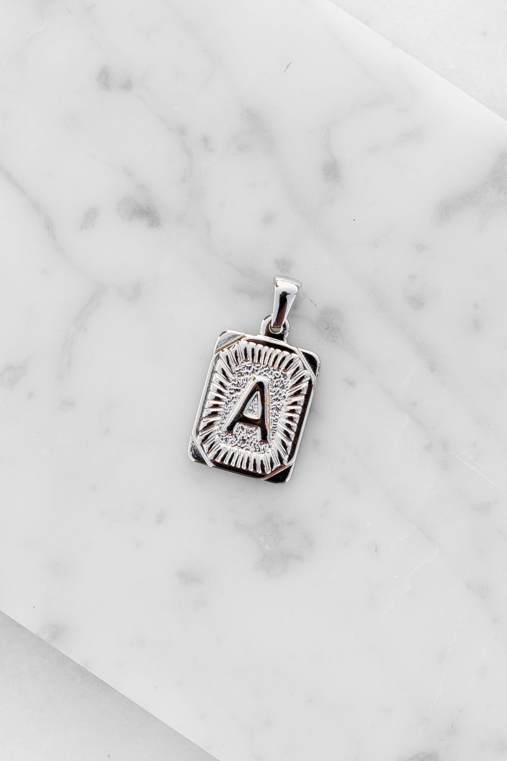 Silver Monogram Letter "A" Charm laying on a marble