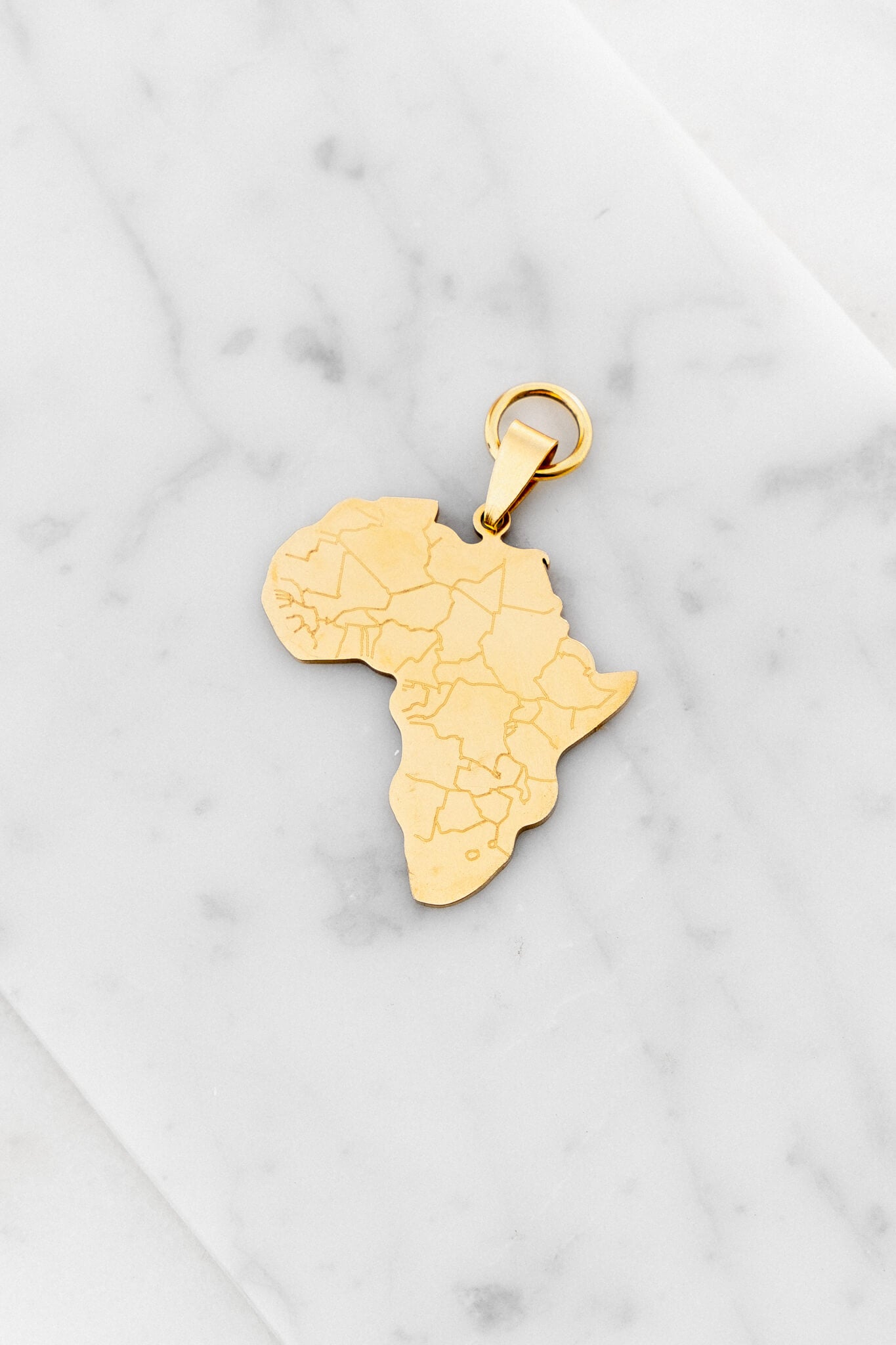 Womankind Africa charm in Gold laying on a marble