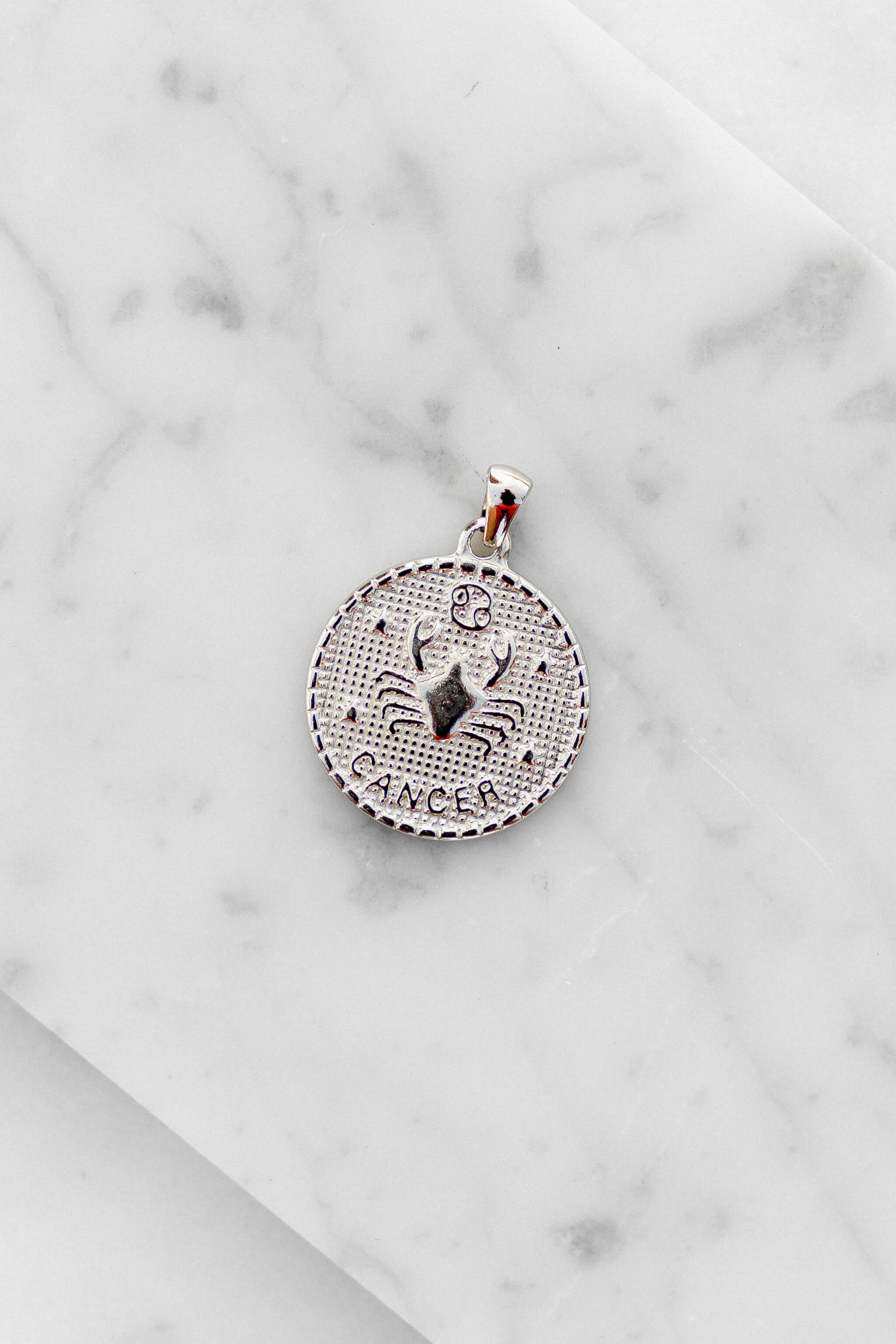 Cancer zodiac sign silver coin charm laying on a white marble