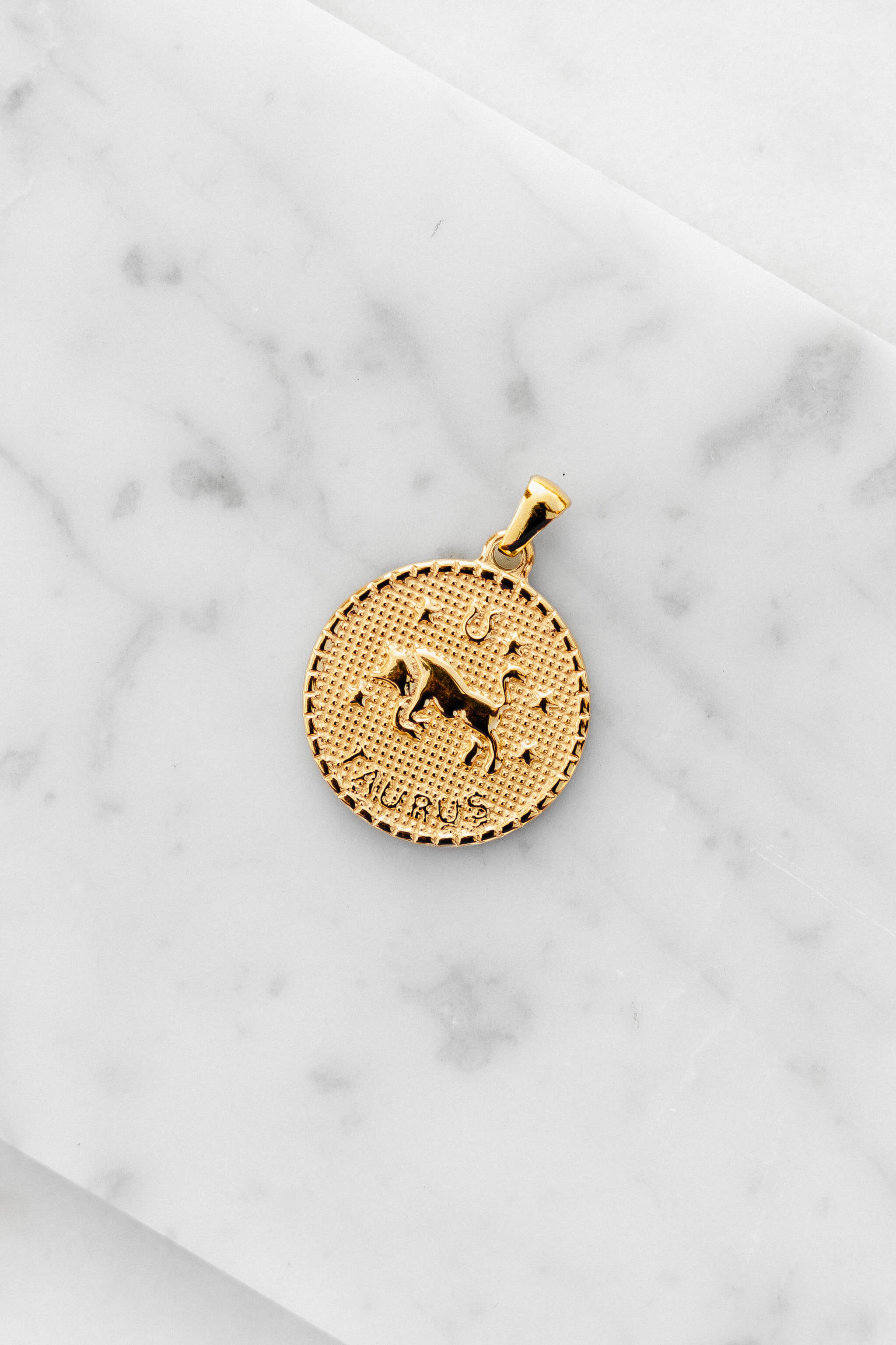 Taurus zodiac sign gold coin charm laying on a white marble