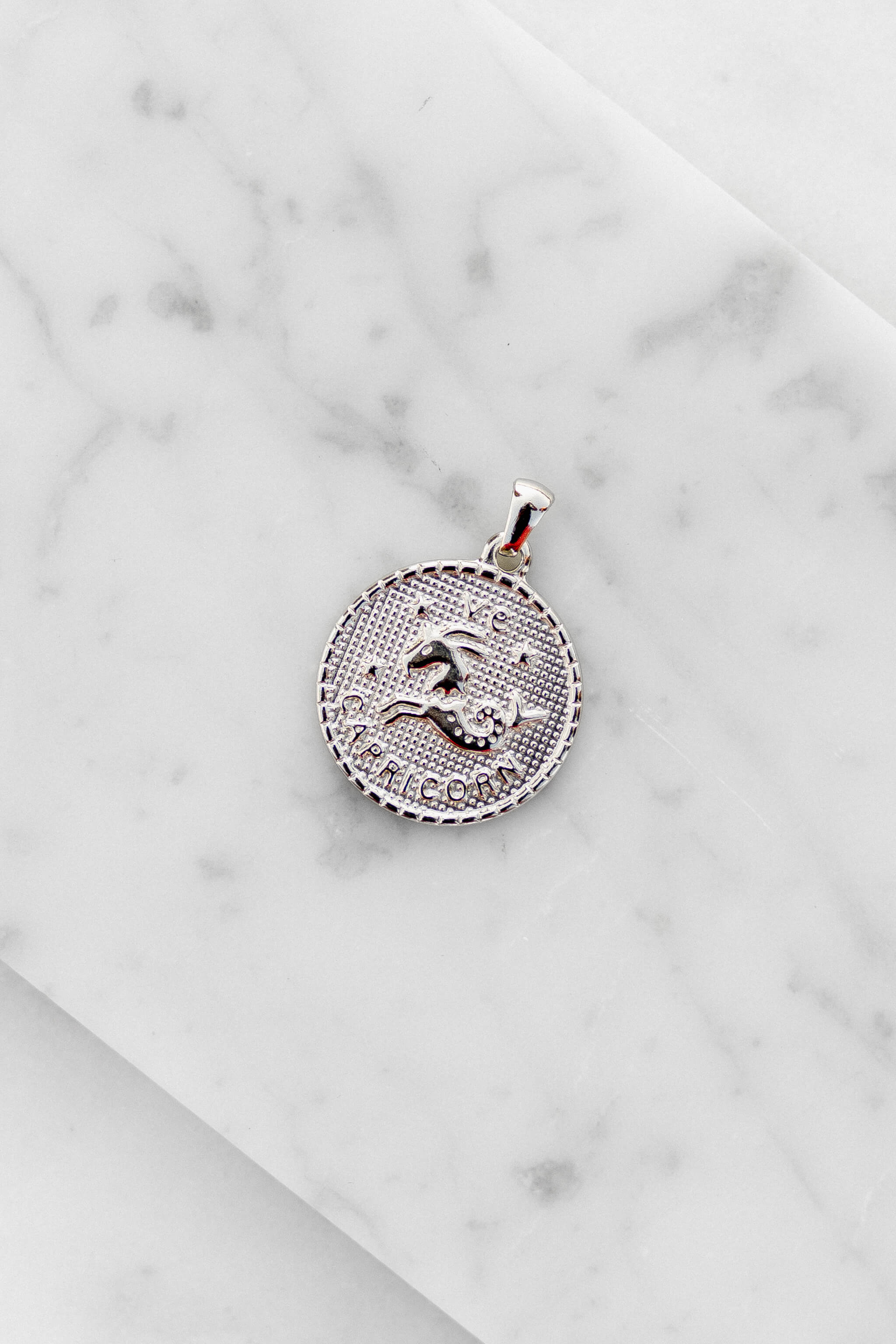 Capricorn zodiac sign silver coin charm laying on a white marble
