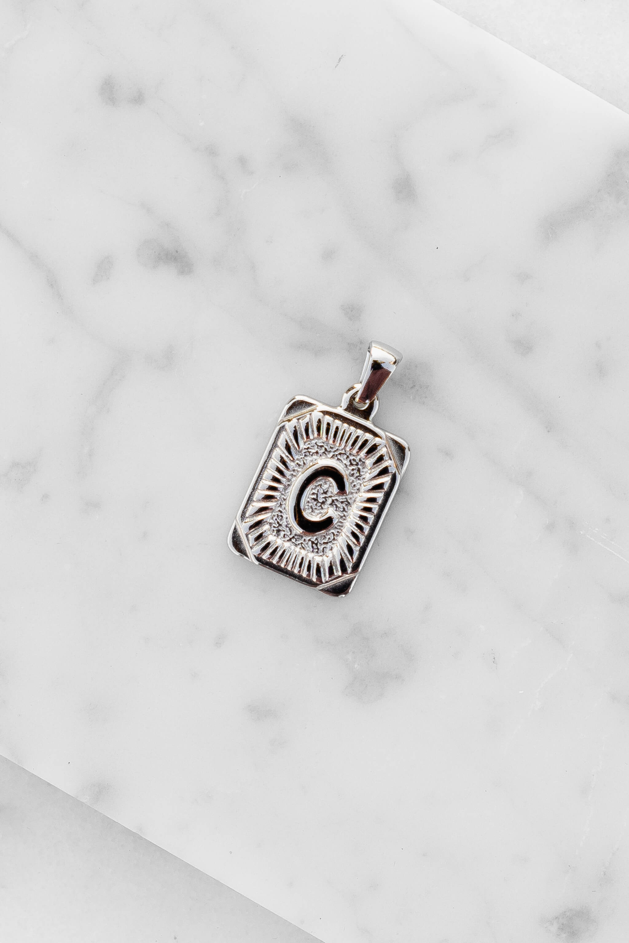 Silver Monogram Letter "C" Charm laying on a marble