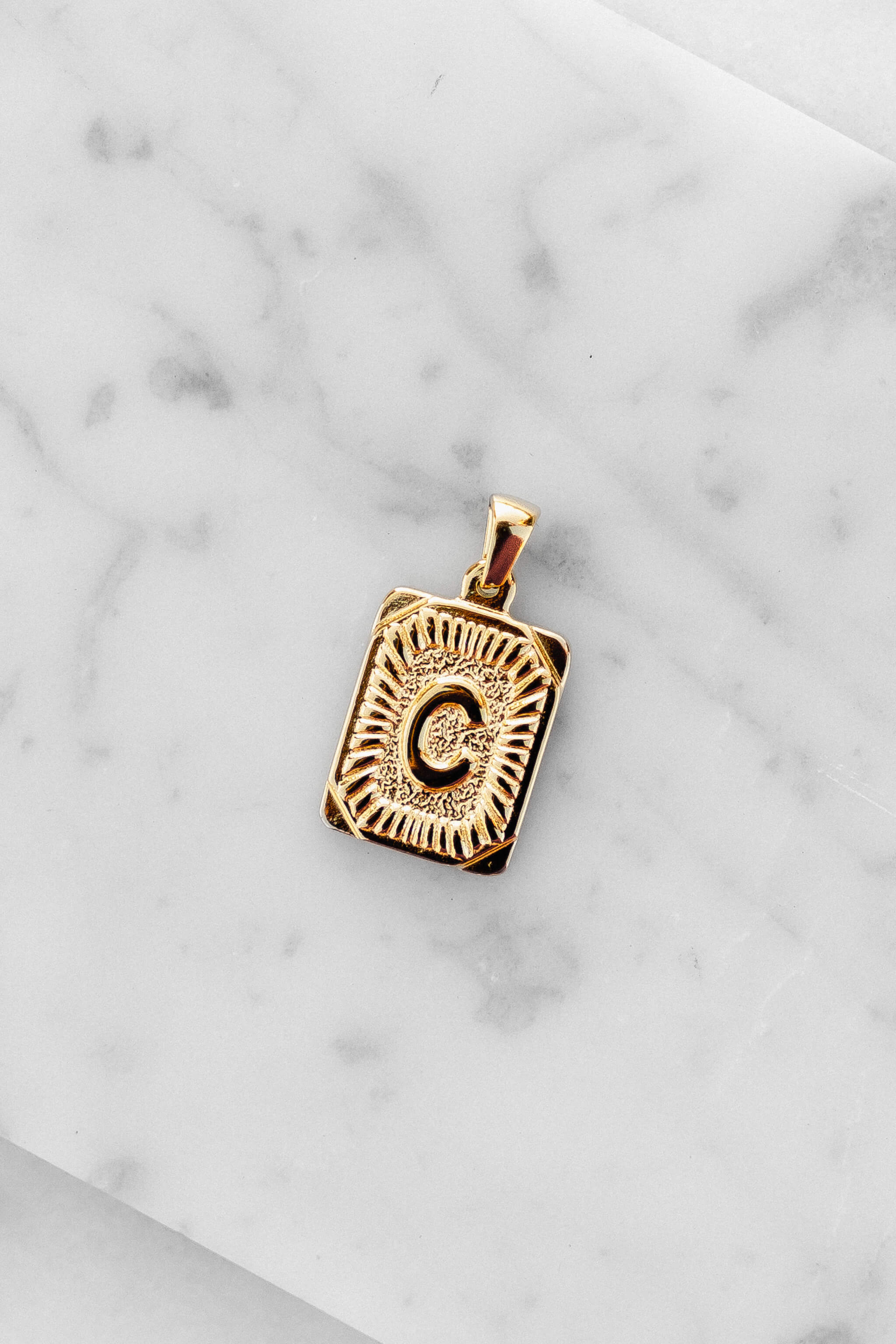 Gold Monogram Letter "C" Charm laying on a marble