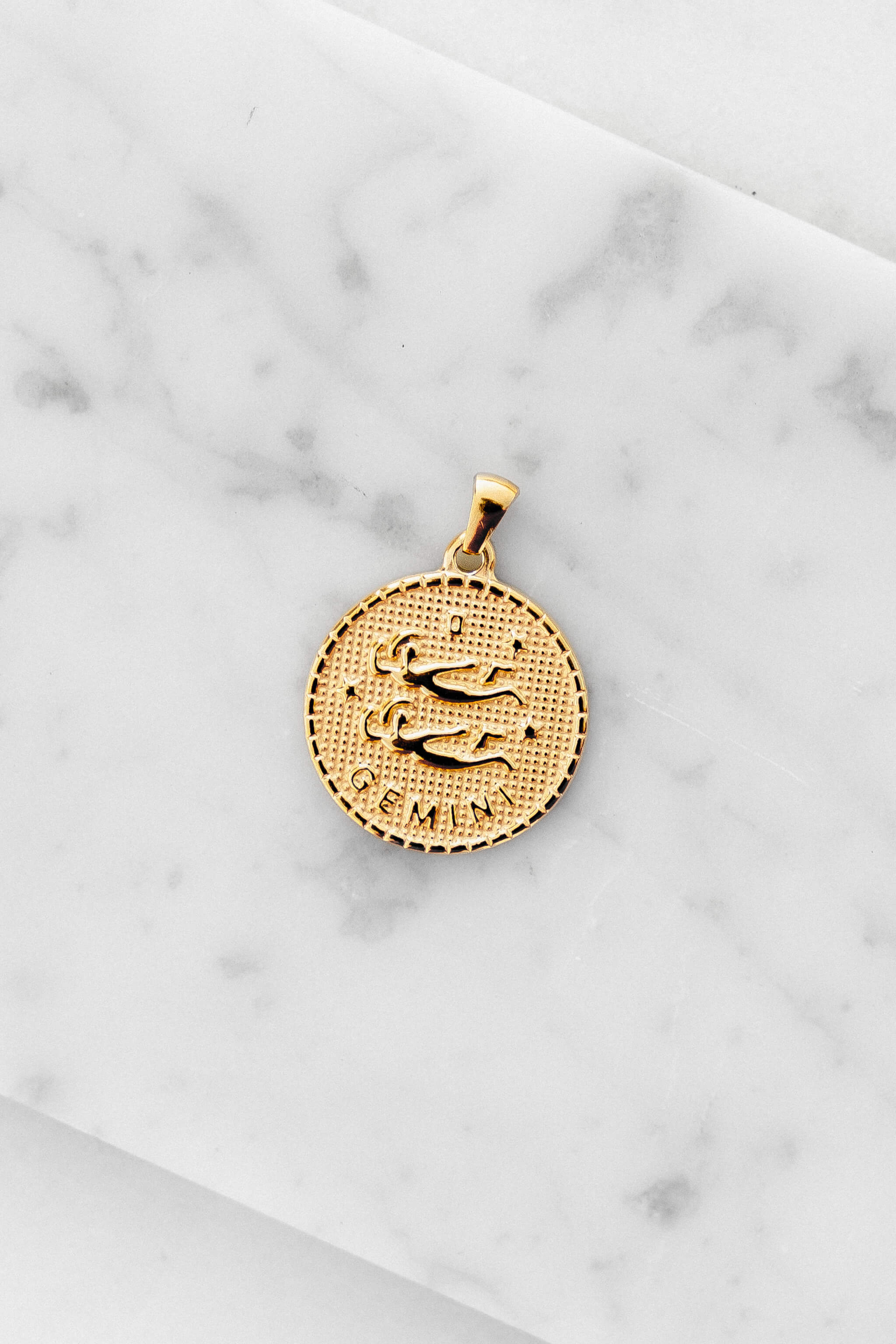 Gemini zodiac sign gold coin charm laying on a white marble