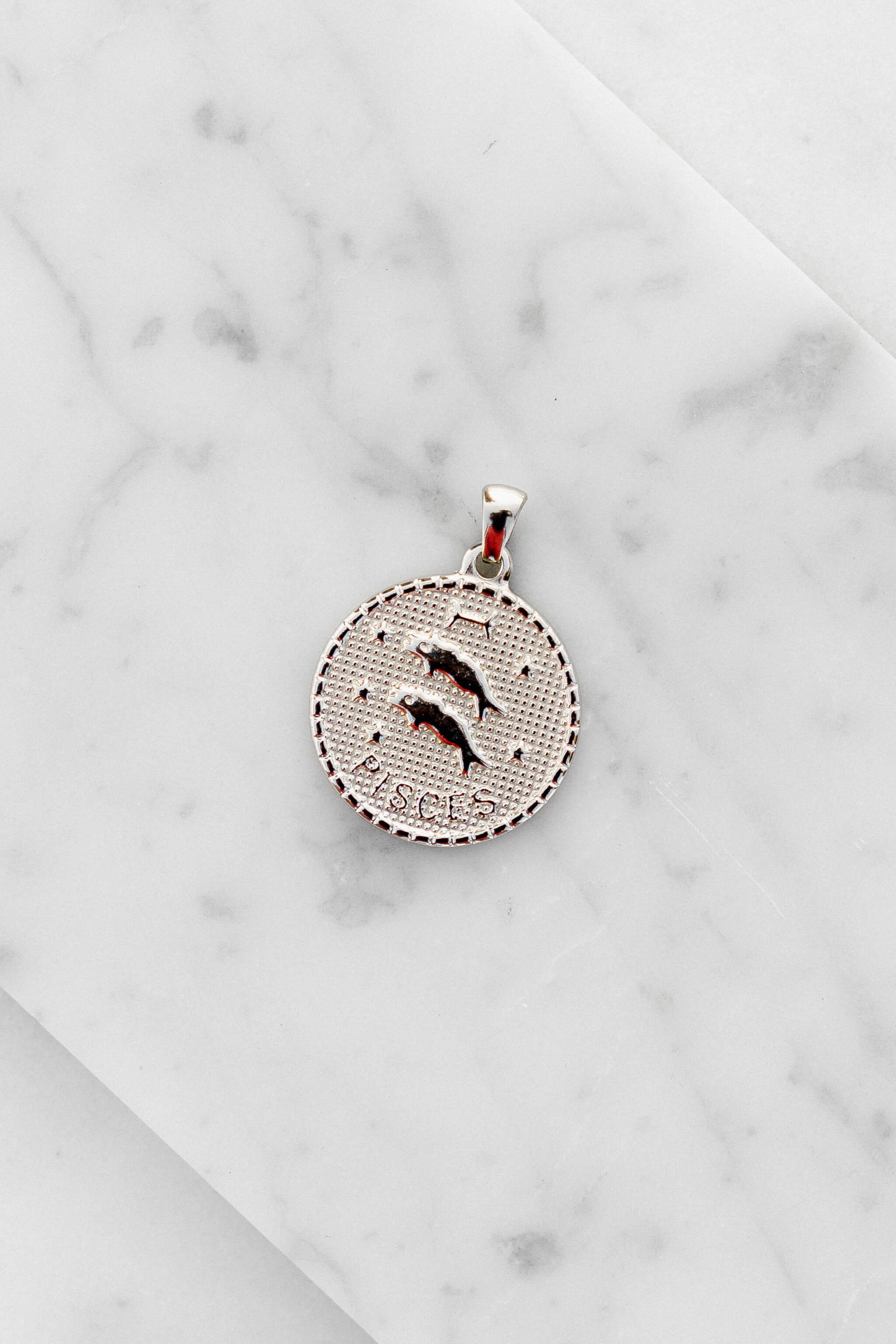 Pisces zodiac sign silver coin charm laying on a white marble