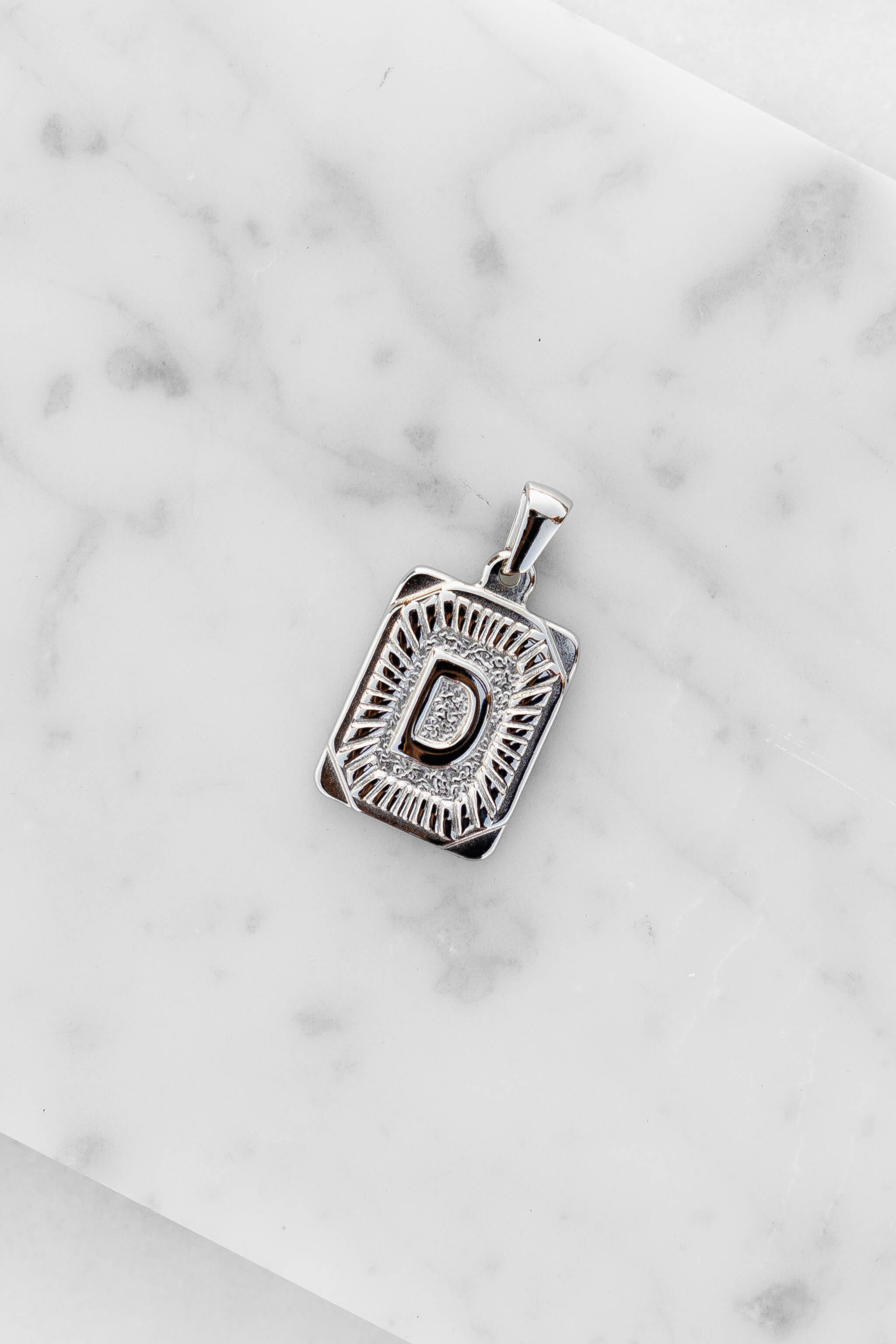 Silver Monogram Letter "D" Charm laying on a marble