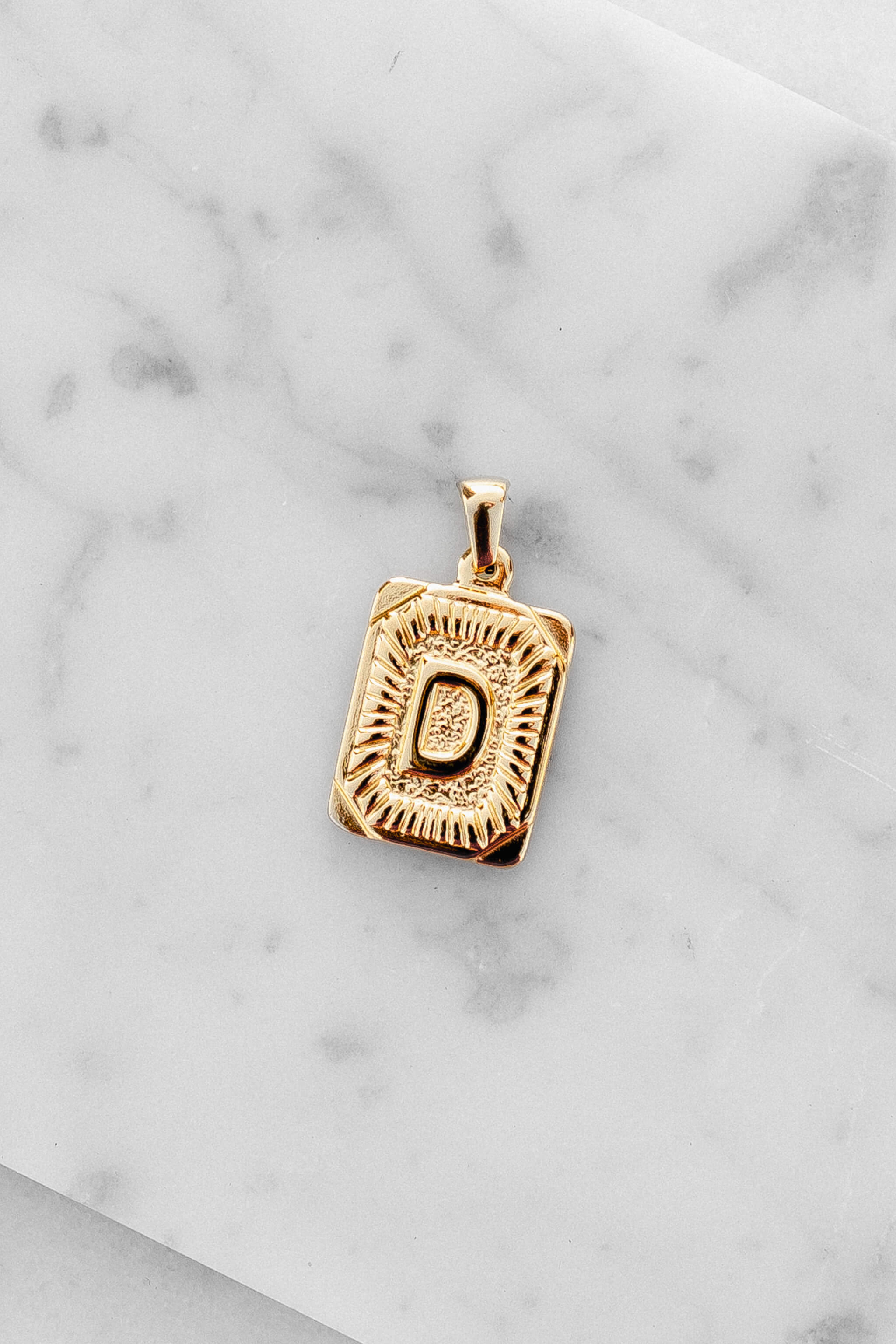 Gold Monogram Letter "D" Charm laying on a marble