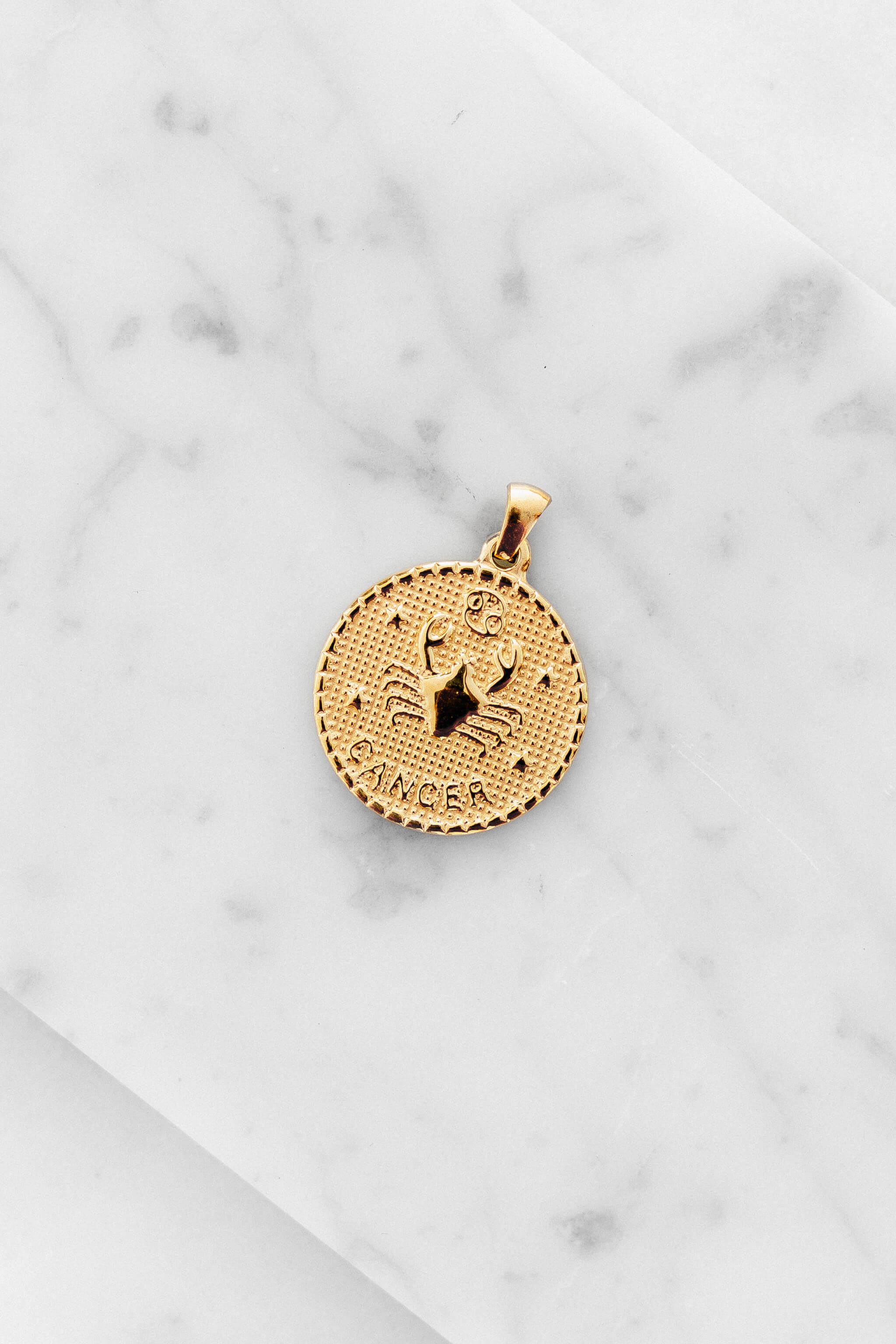 Cancer zodiac sign gold coin charm laying on a white marble
