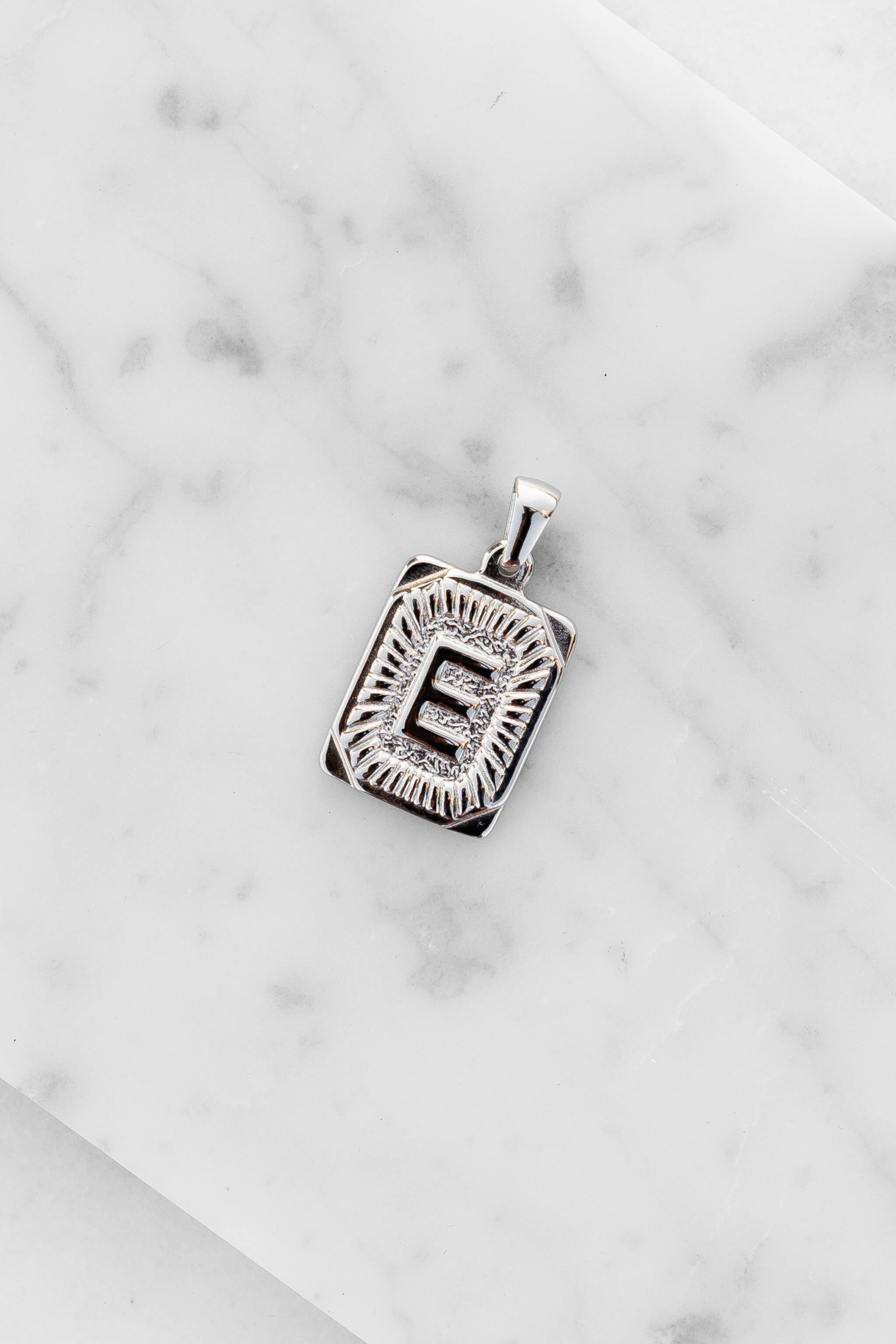 Silver Monogram Letter "E" Charm laying on a marble
