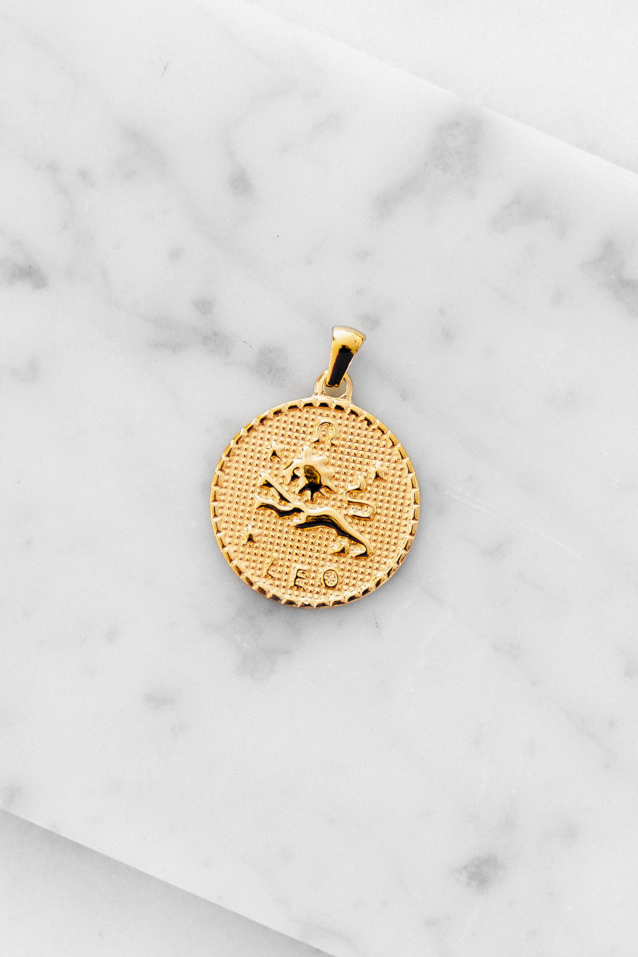 Leo zodiac sign gold coin charm laying on a white marble
