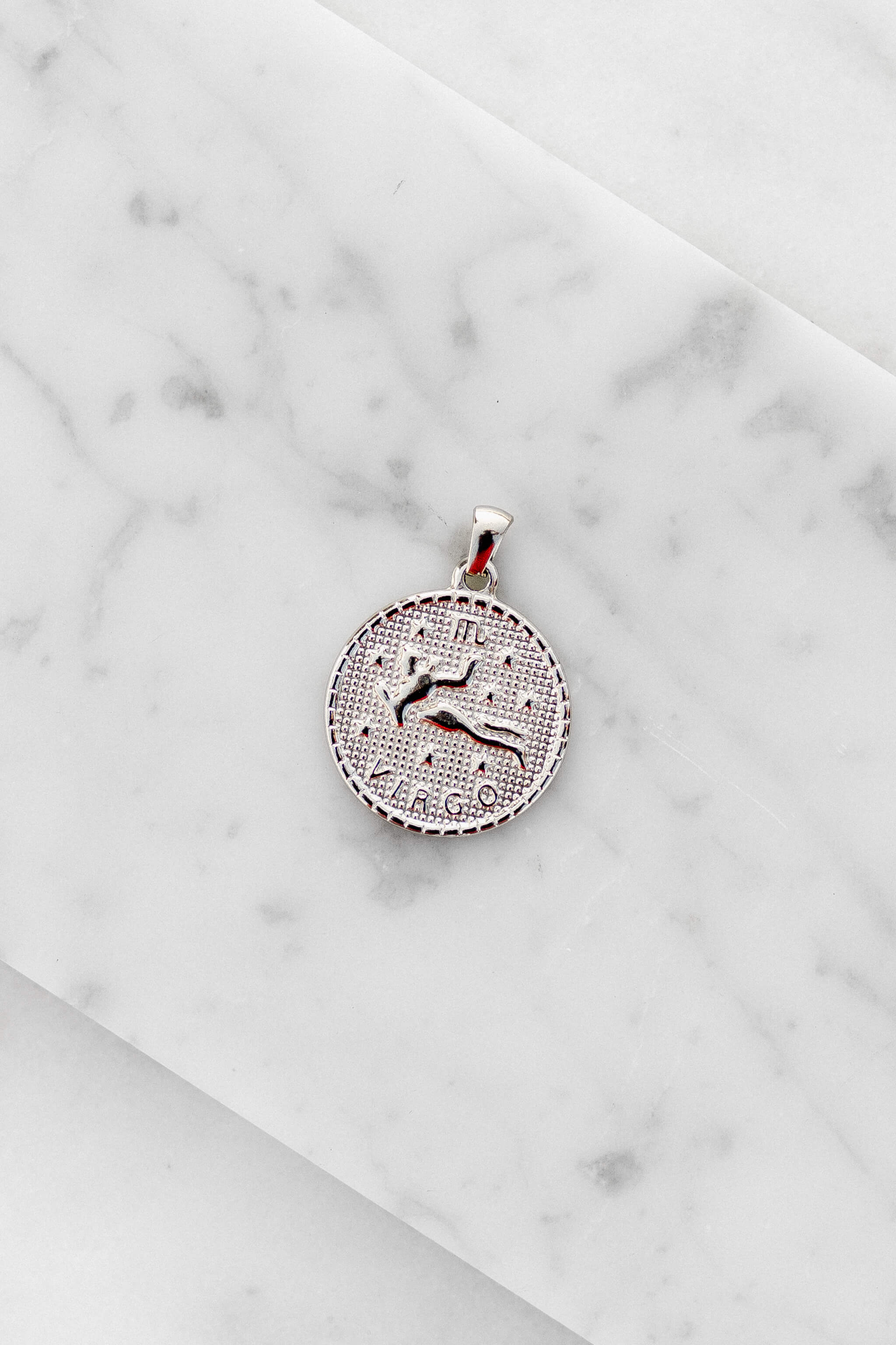 Virgo zodiac sign silver coin charm laying on a white marble