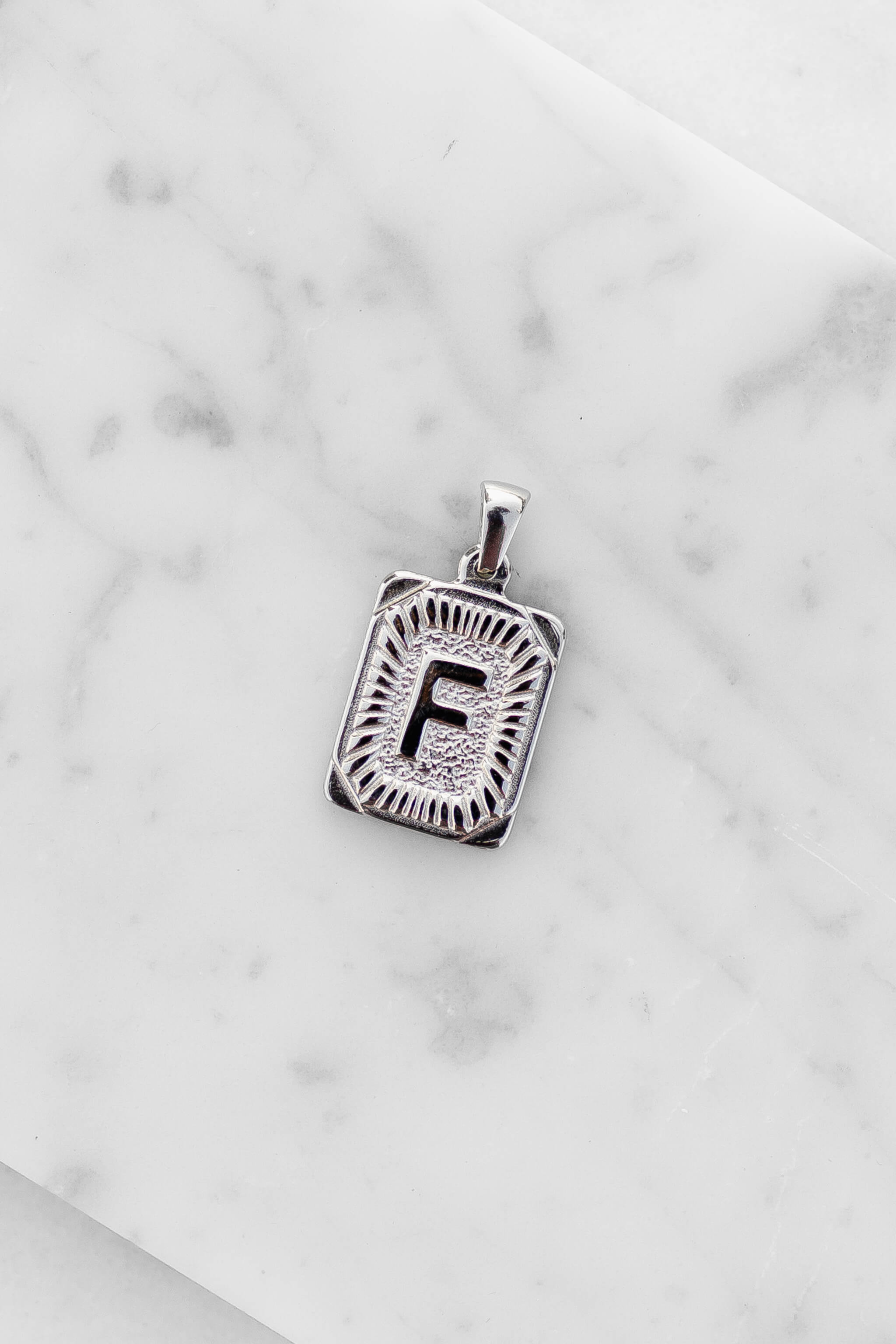 Silver Monogram Letter "F" Charm laying on a marble
