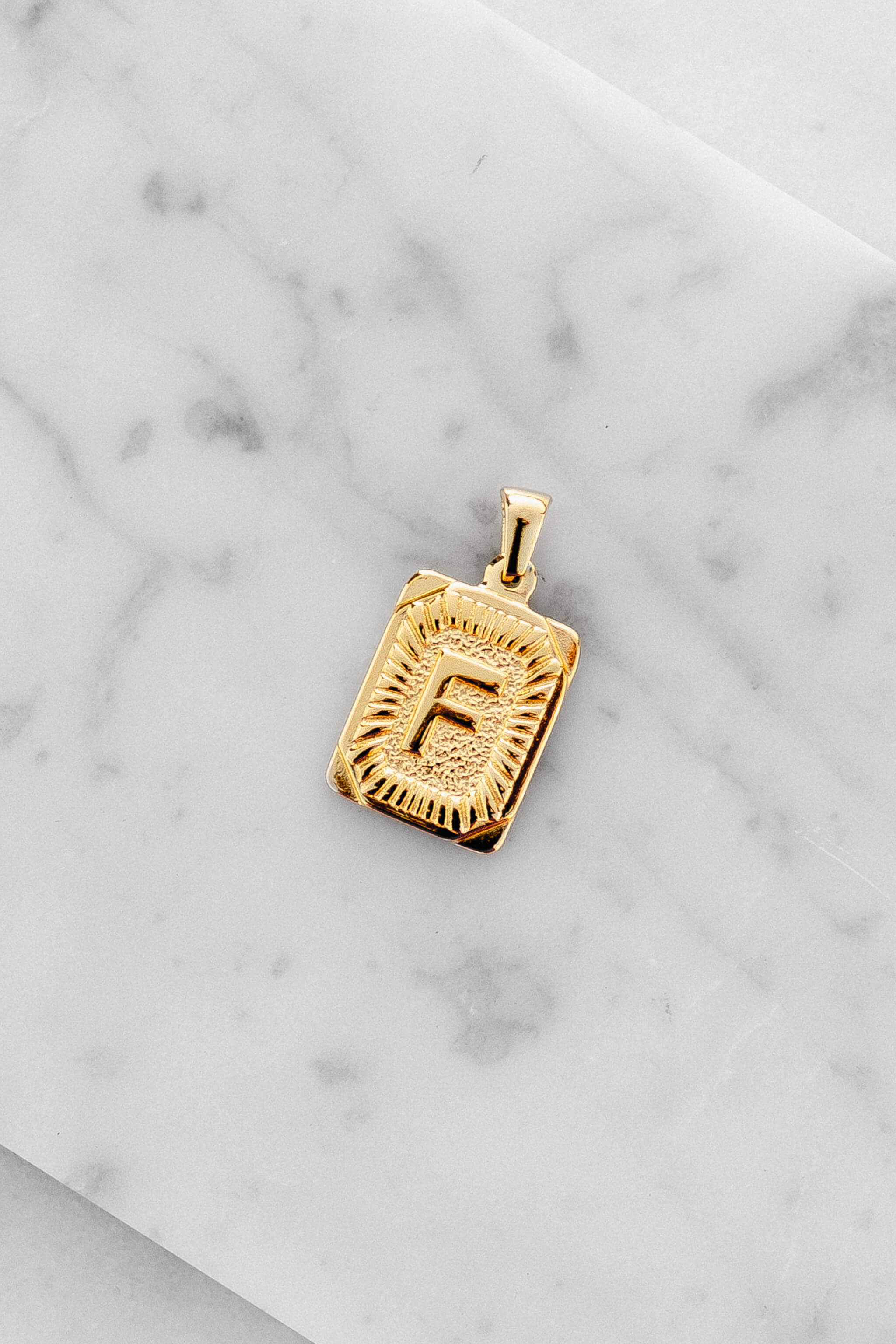 Gold Monogram Letter "F" Charm laying on a marble