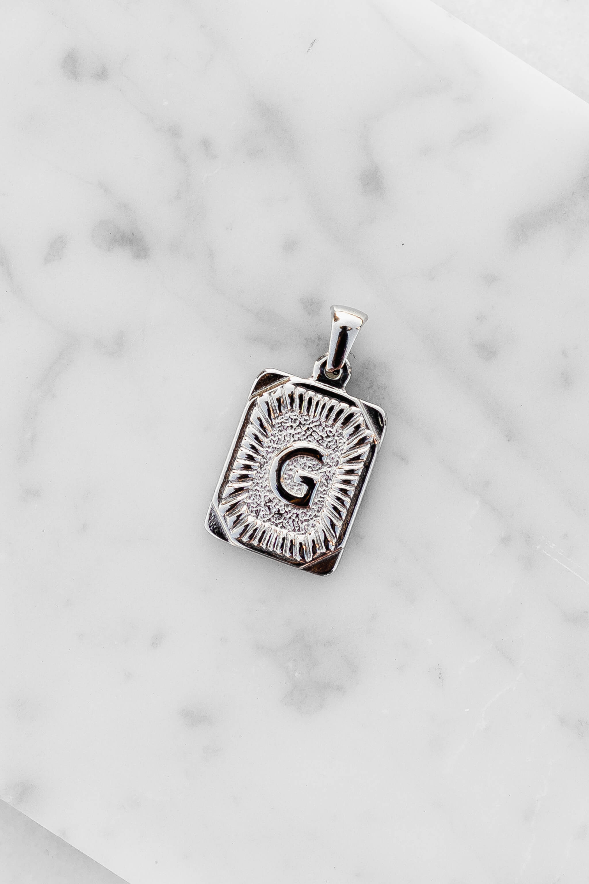 Silver Monogram Letter "G" Charm laying on a marble