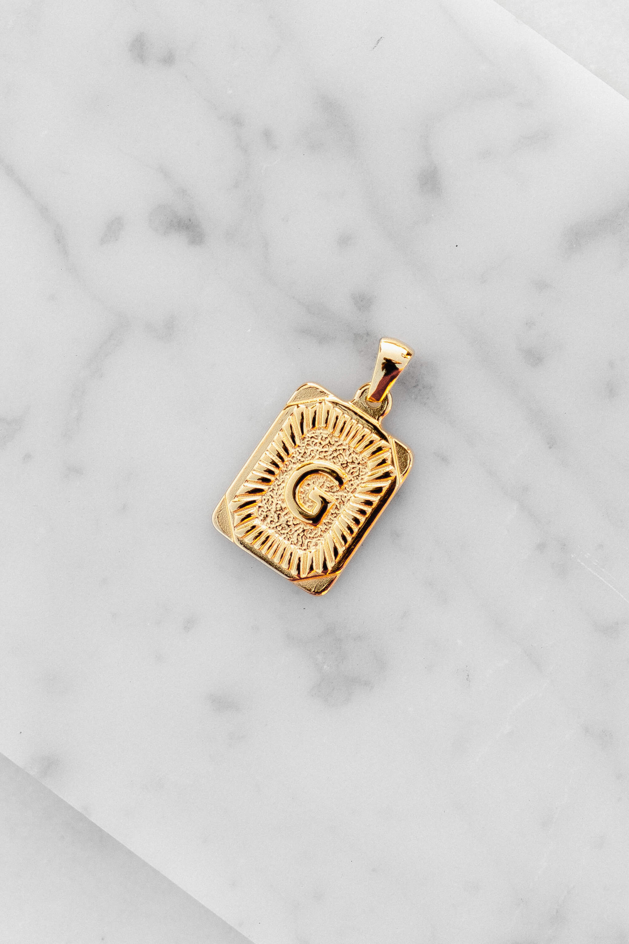 Gold Monogram Letter "G" Charm laying on a marble