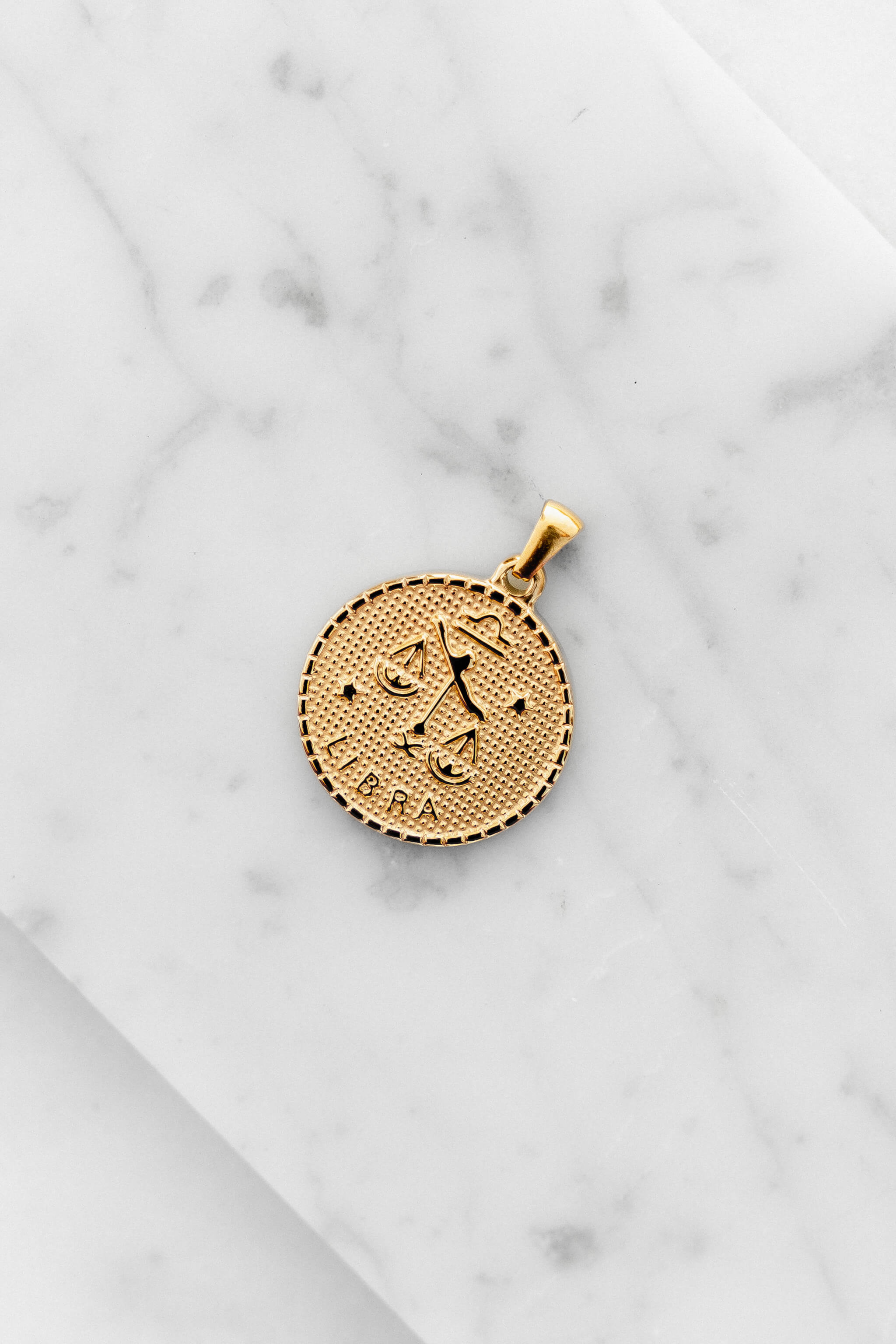 Libra zodiac sign gold coin charm laying on a white marble