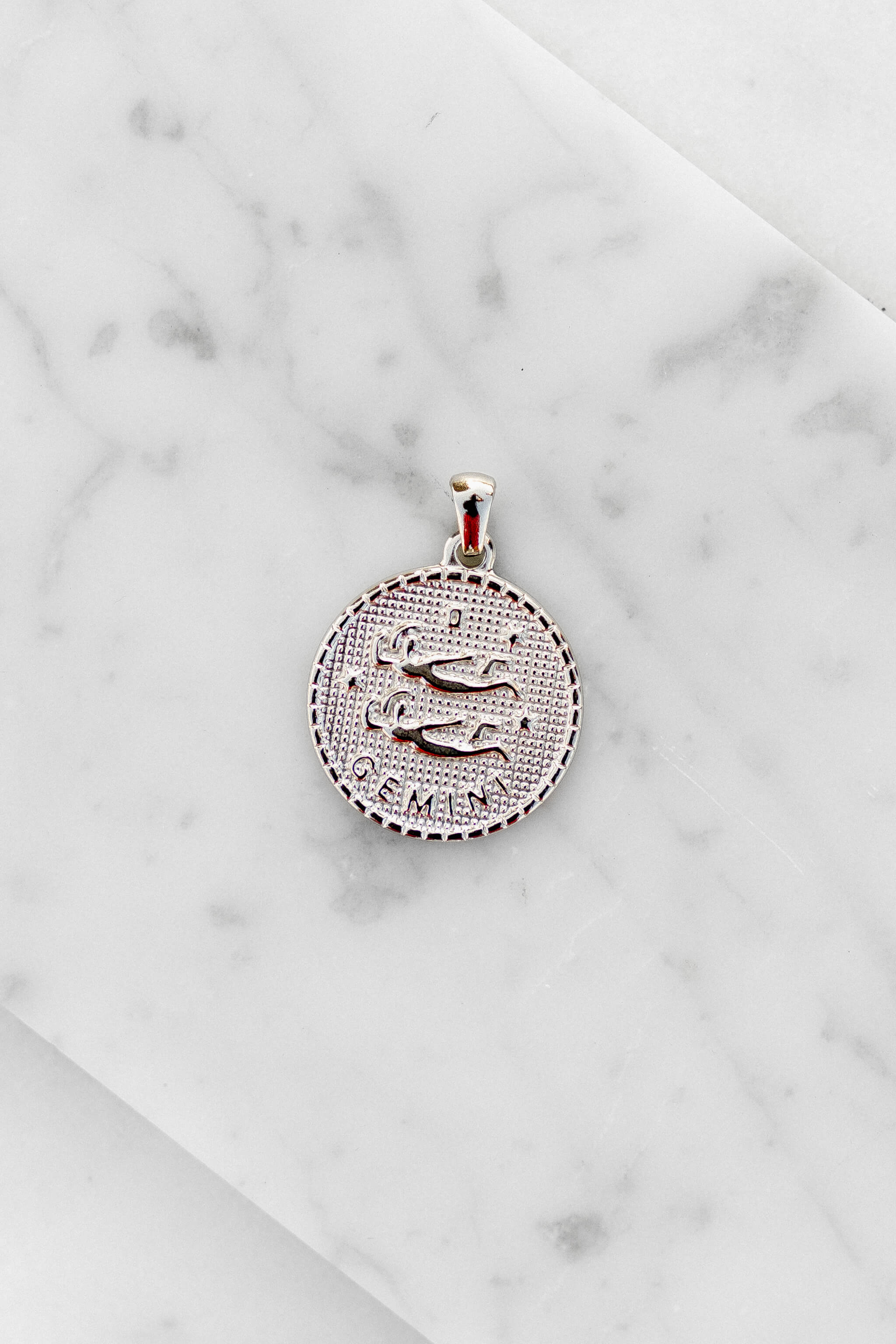 Gemini zodiac sign silver coin charm laying on a white marble