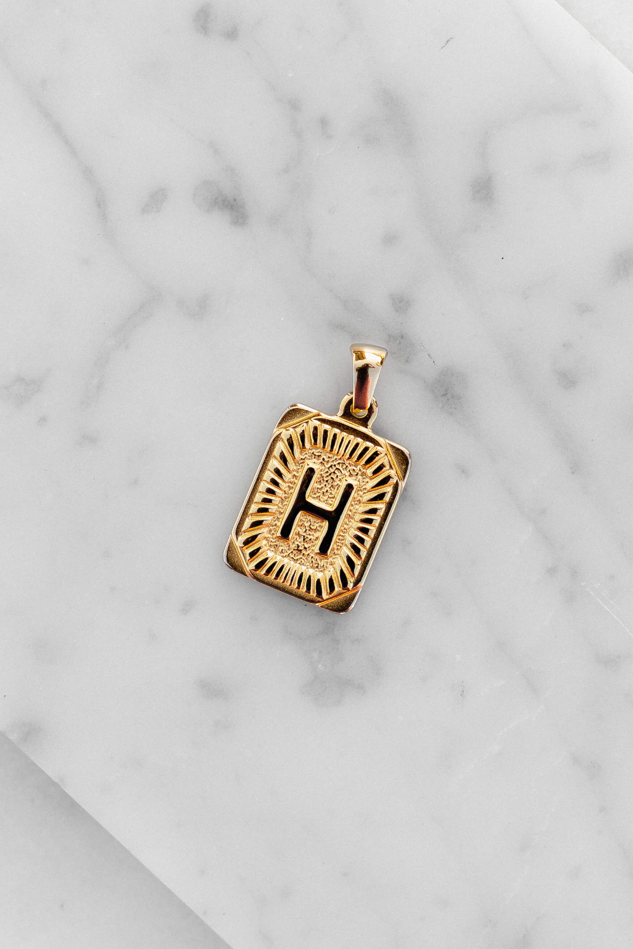 Gold Monogram Letter "H" Charm laying on a marble