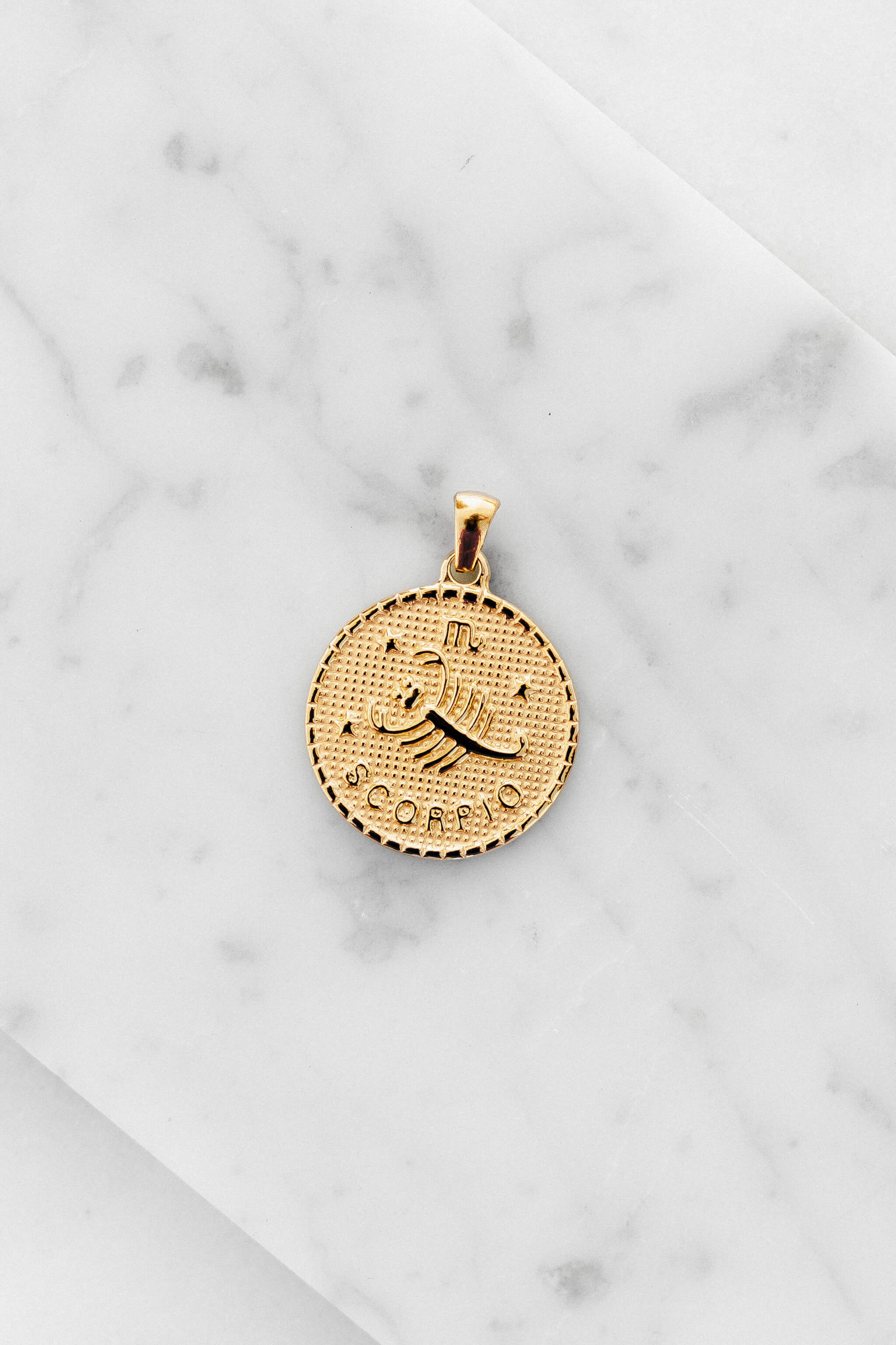 Scorpio zodiac sign gold coin charm laying on a white marble