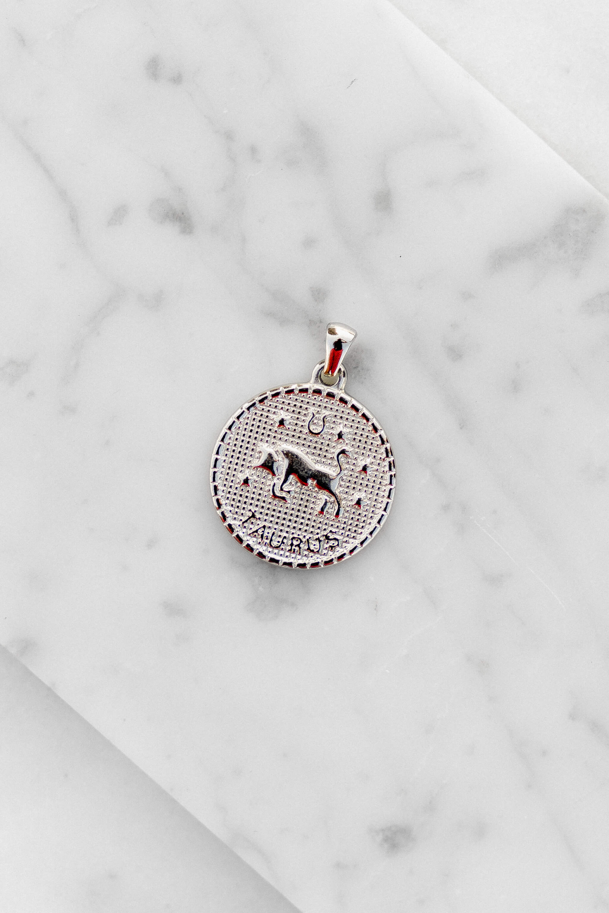 Taurus zodiac sign silver coin charm laying on a white marble