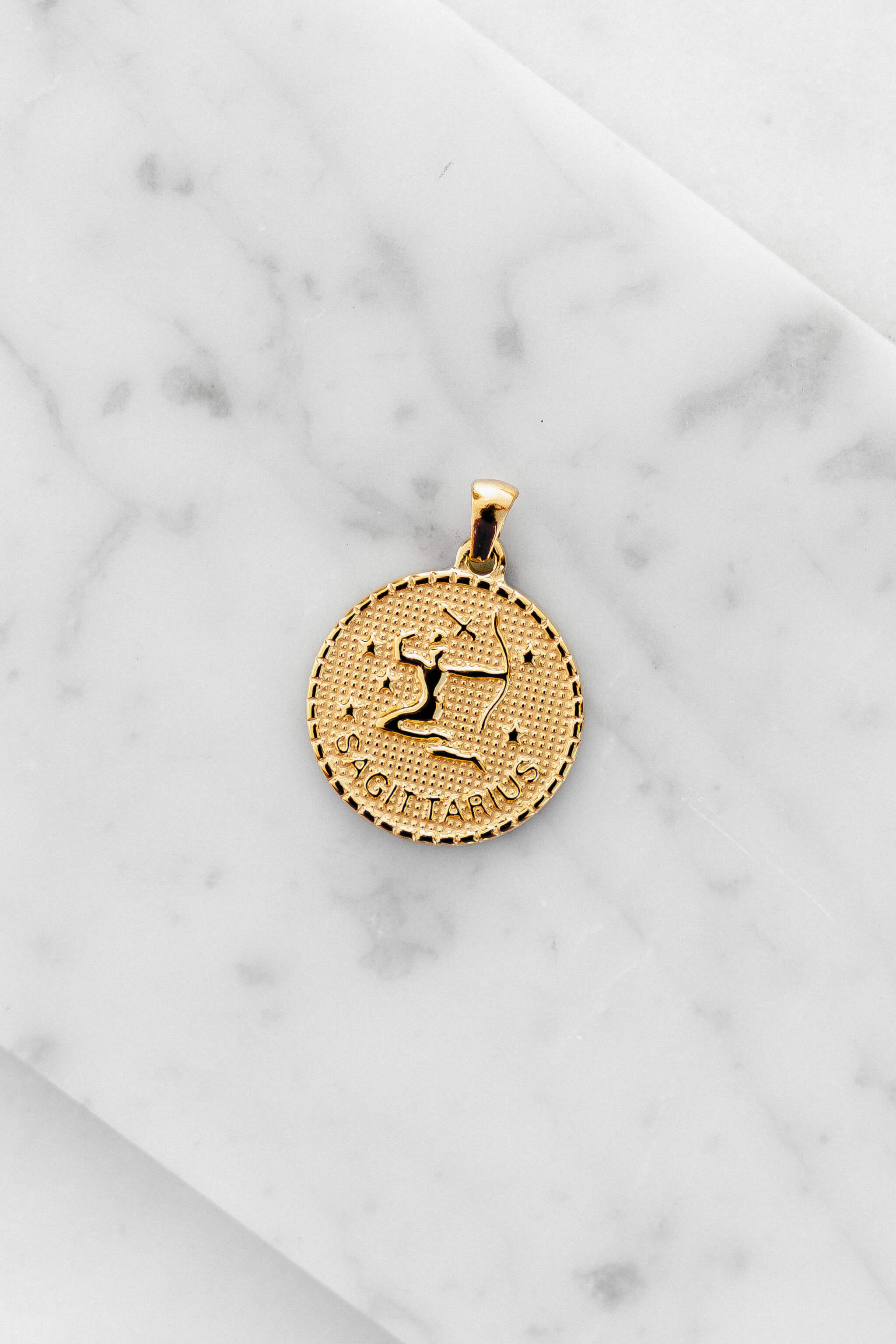 Sagittarius zodiac sign gold coin charm laying on a white marble