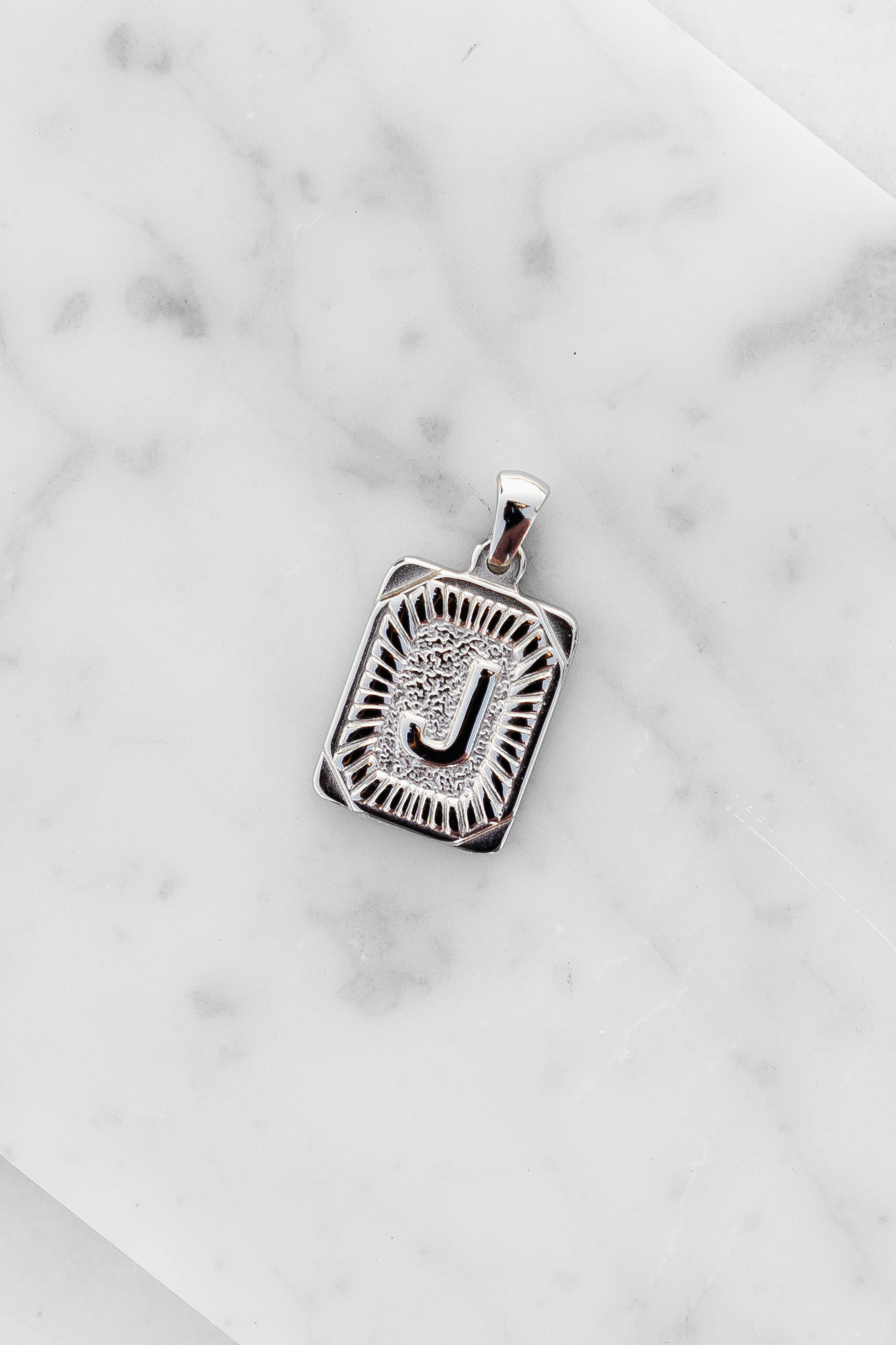 Silver Monogram Letter "J" Charm laying on a marble