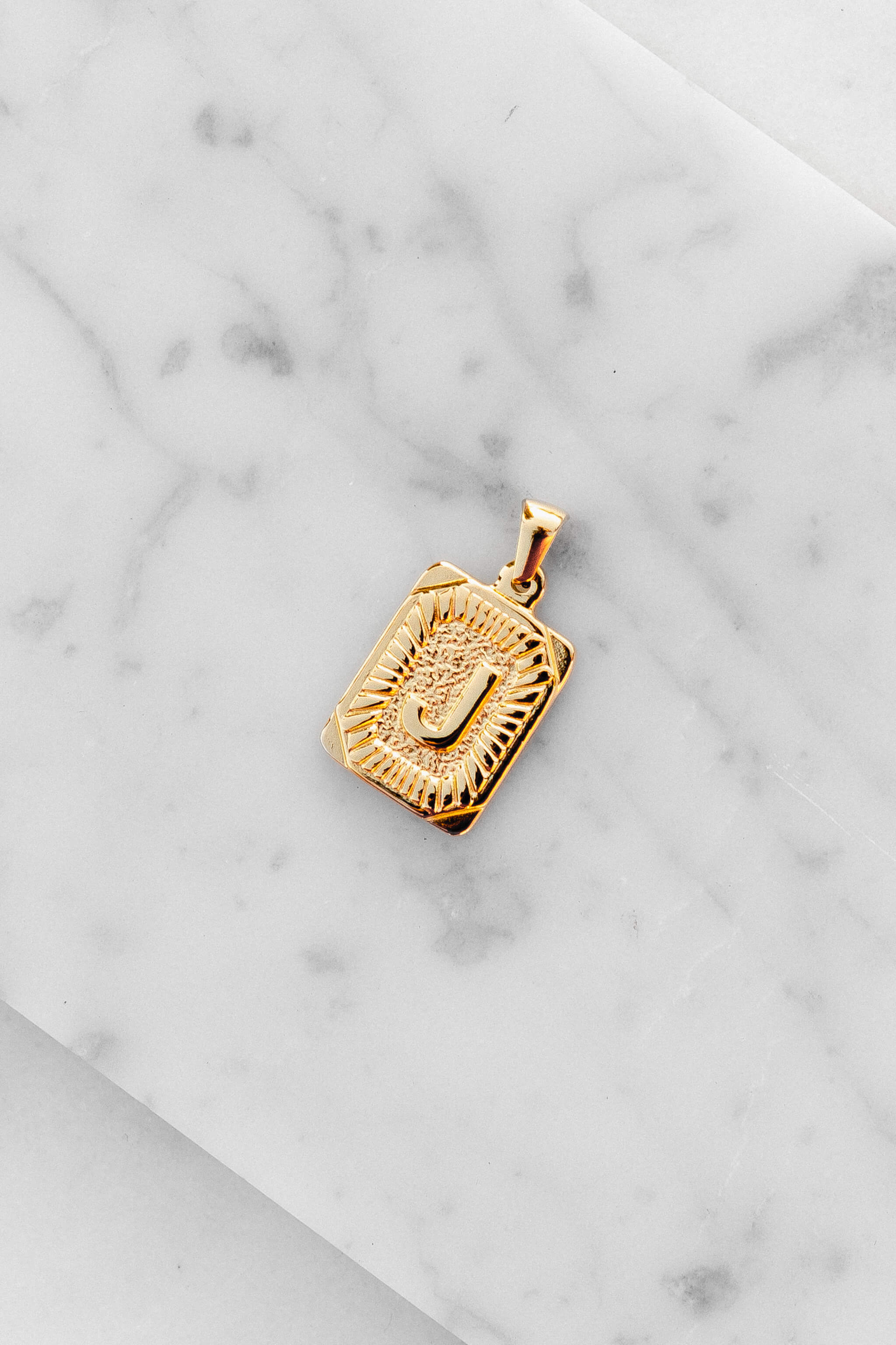Gold Monogram Letter "J" Charm laying on a marble
