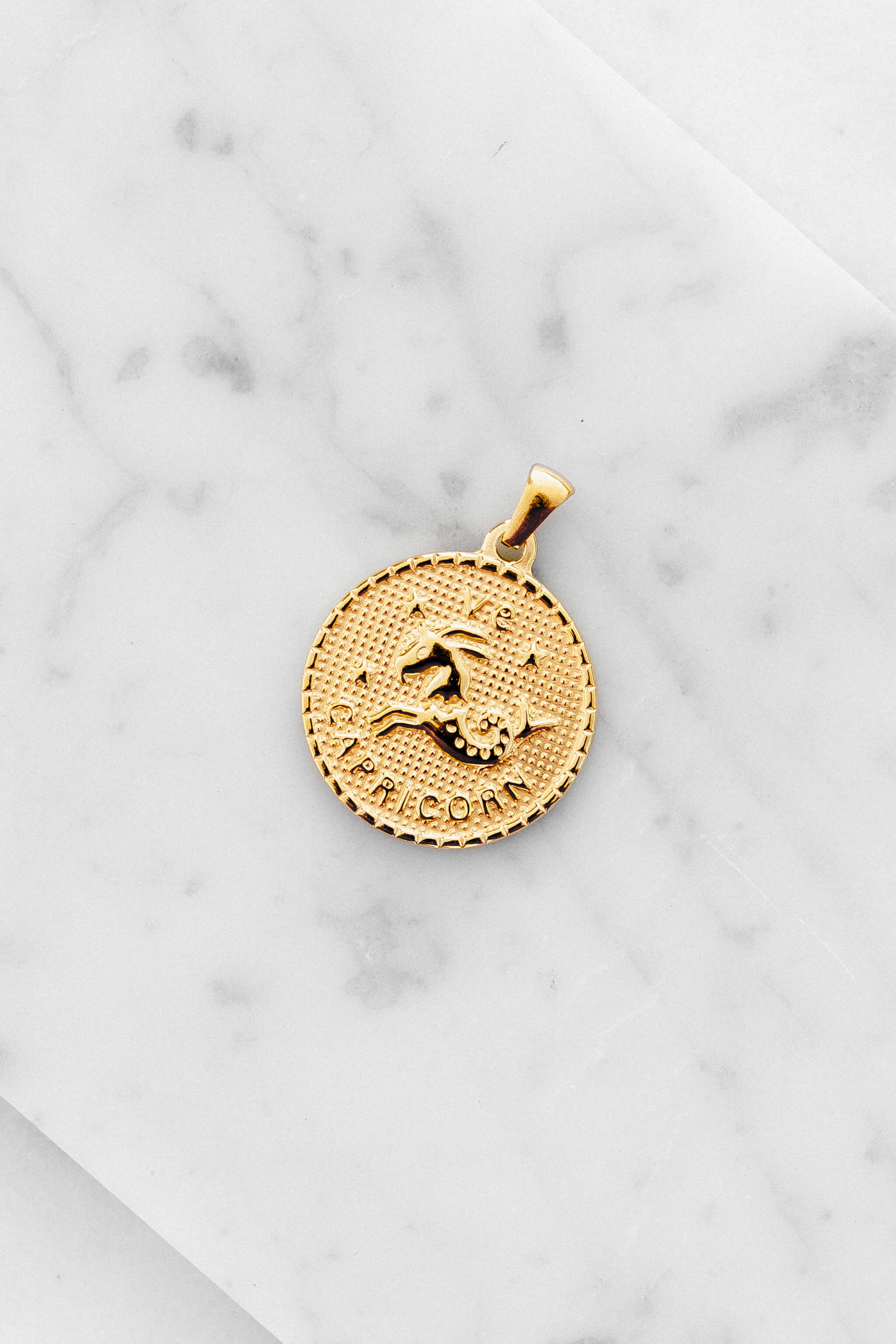 Capricorn zodiac sign gold coin charm laying on a white marble